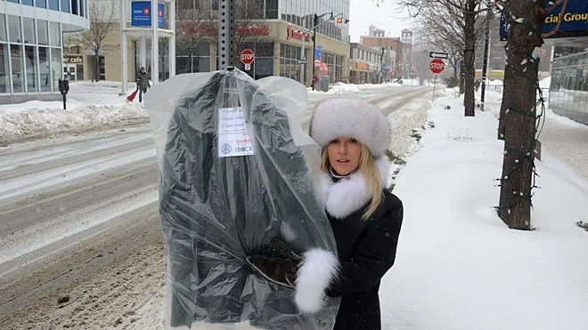 Joanna L. Cox hanging a winter coat on a downtown Sudbury street pole during the Random Acts of Kindness project, providing free warm clothing for those in need.