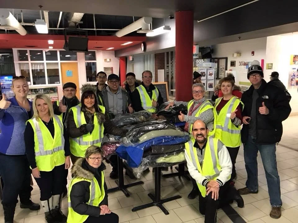 Rotarians posing with coats to hang on poles for coats and coffee initiative with Joanna Cox