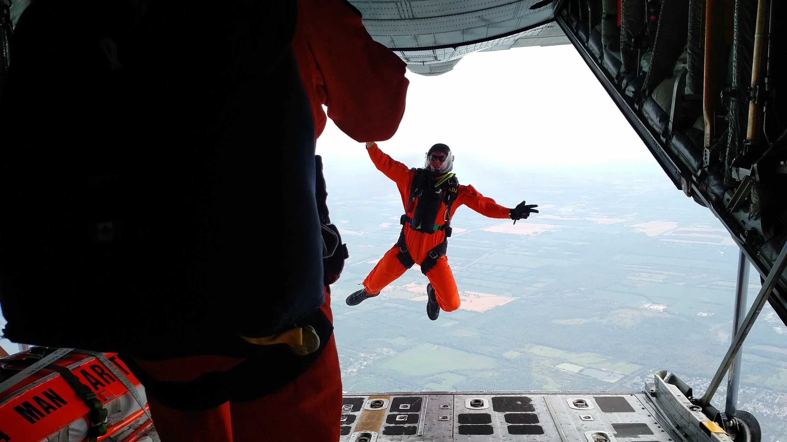 Canadian SAR Tech in bright orange suit performing a parachute jump from a Royal Canadian Air Force aircraft as part of a search and rescue training mission.
