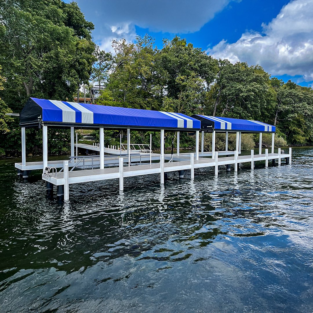 A floating dock with two covered sections on a lake, surrounded by trees and a partly cloudy sky.