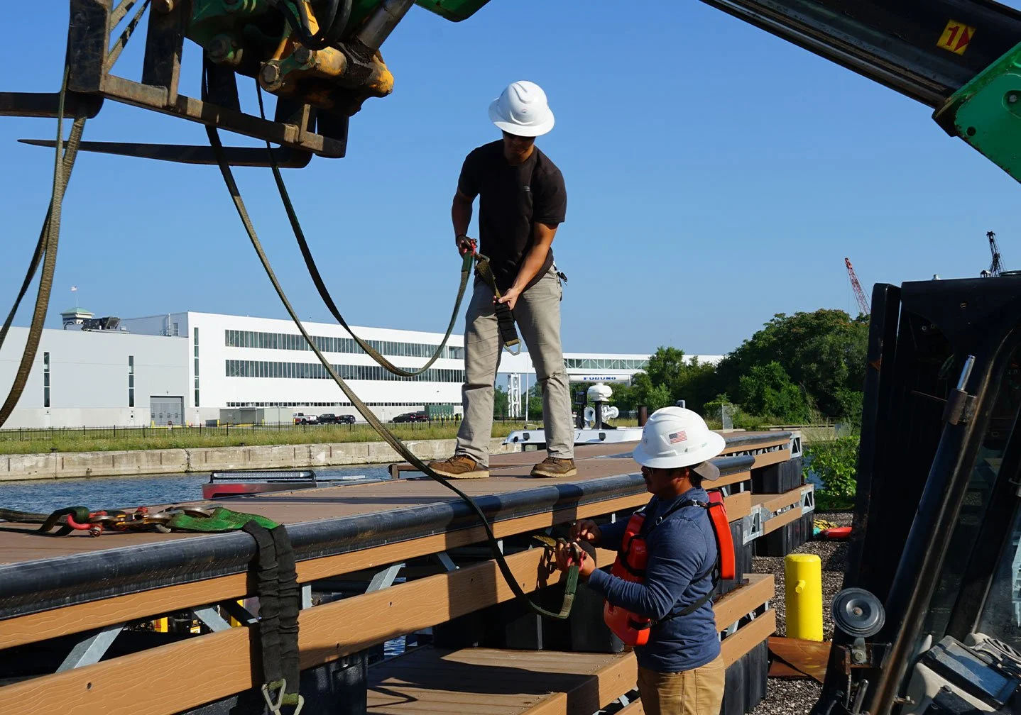   Crane-Assisted Pier Placement:  
A crane lifts and positions a pier section into place while crew members guide alignment and ensure proper installation on the waterfront structure. 