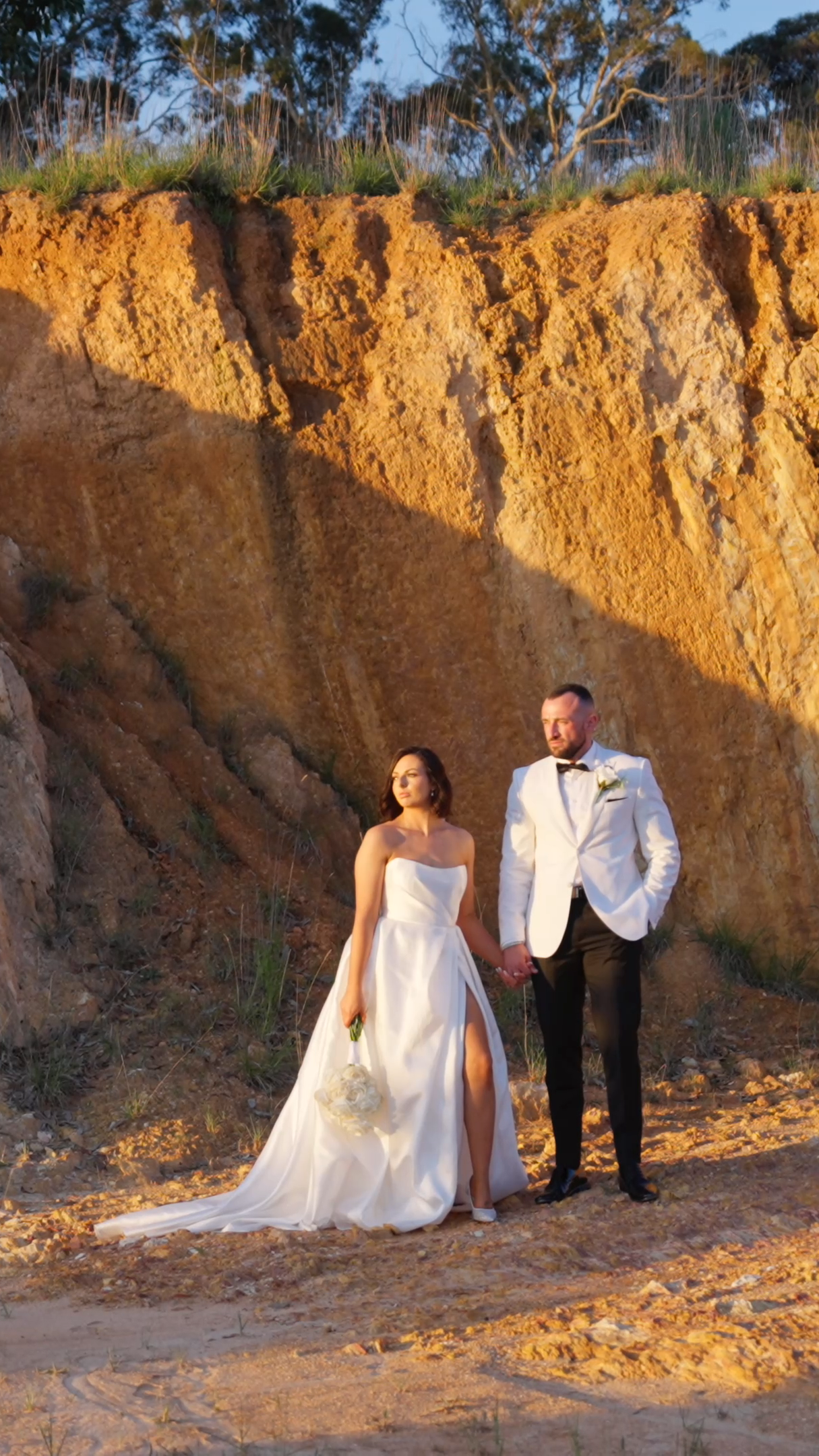 Bride and groom holding hands at the rock wall at LOT.100, Hay Valley, in golden hour light