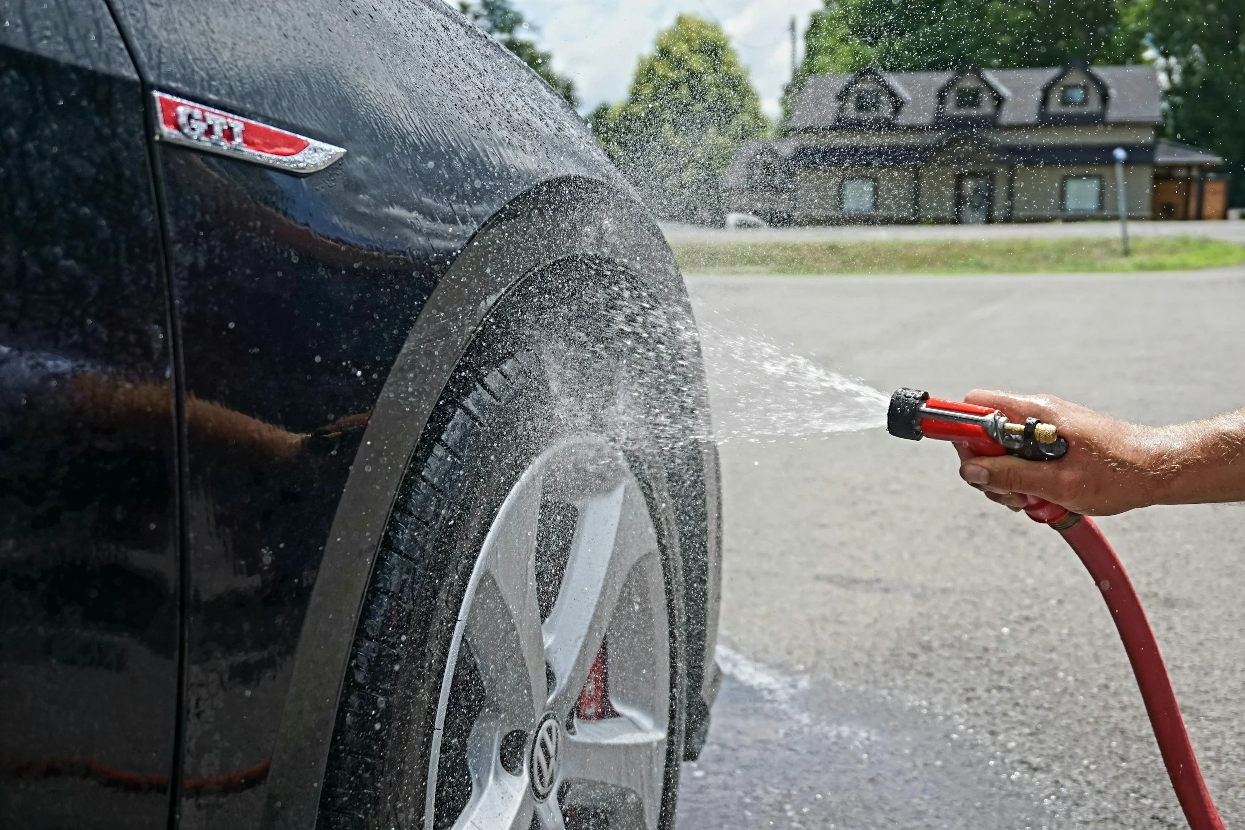 Close-up of a car being rinsed with a hose during a professional mobile car detailing service.