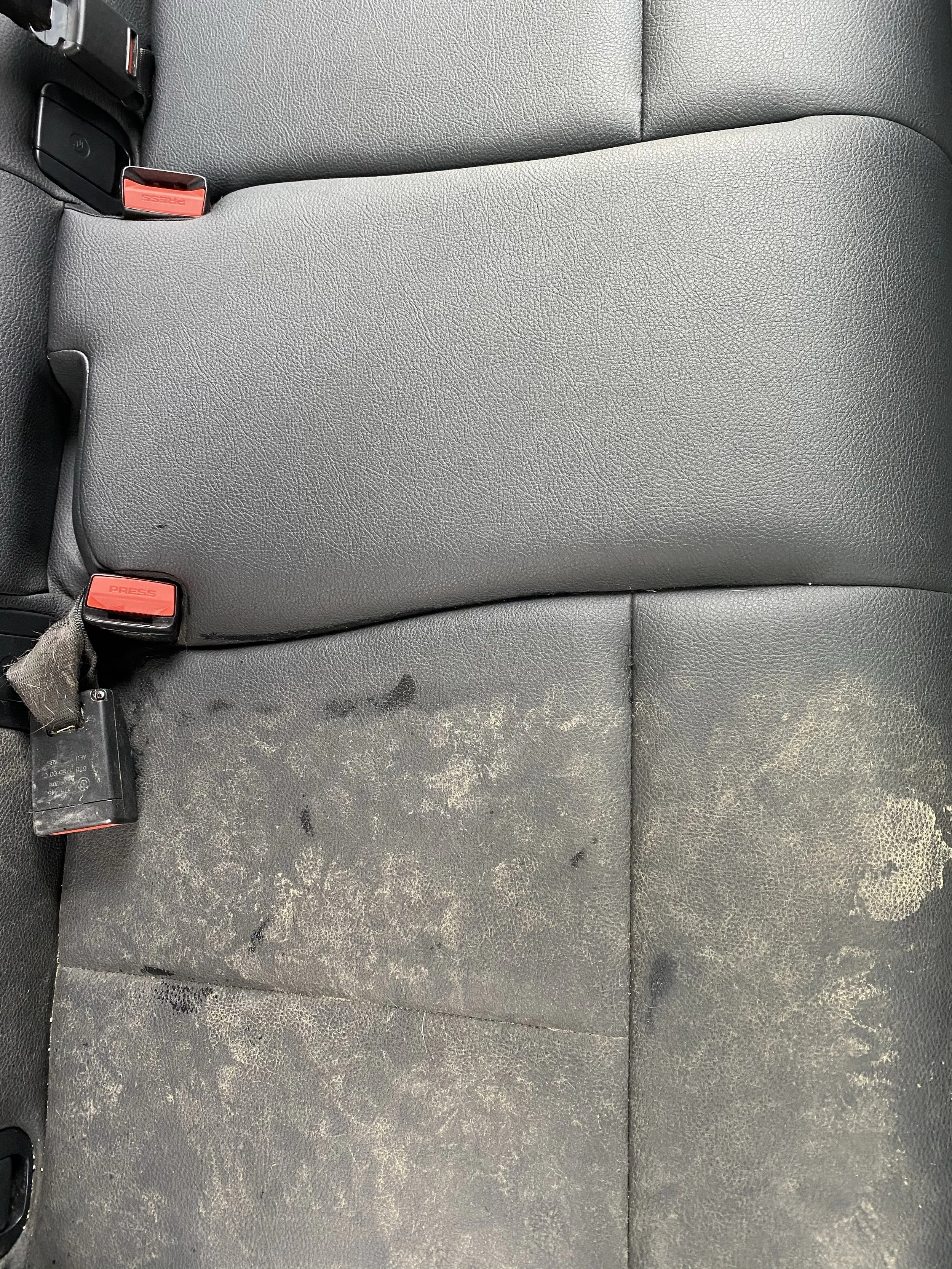 Car seat with worn, stained fabric and two red seatbelt buckles.