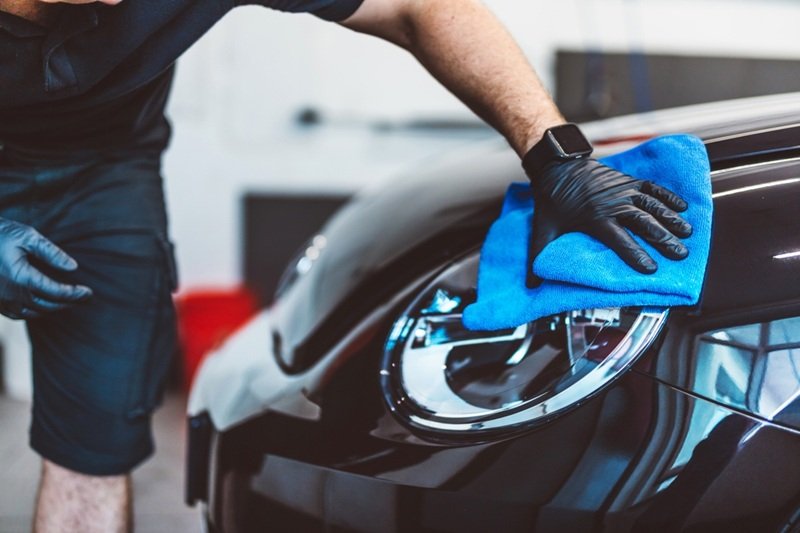 alt="Auto detailing technician cleaning a car headlight with a blue microfiber towel during a professional mobile car detailing service in Everett, Washington."