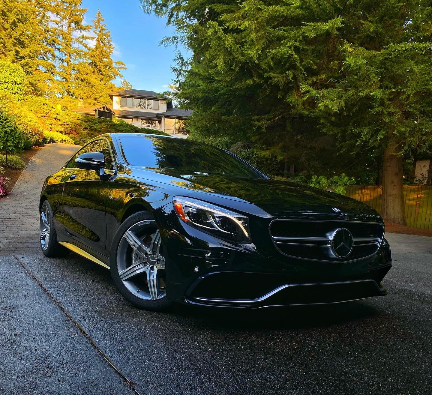 Black Mercedes-Benz convertible parked on a residential driveway surrounded by trees and greenery. 