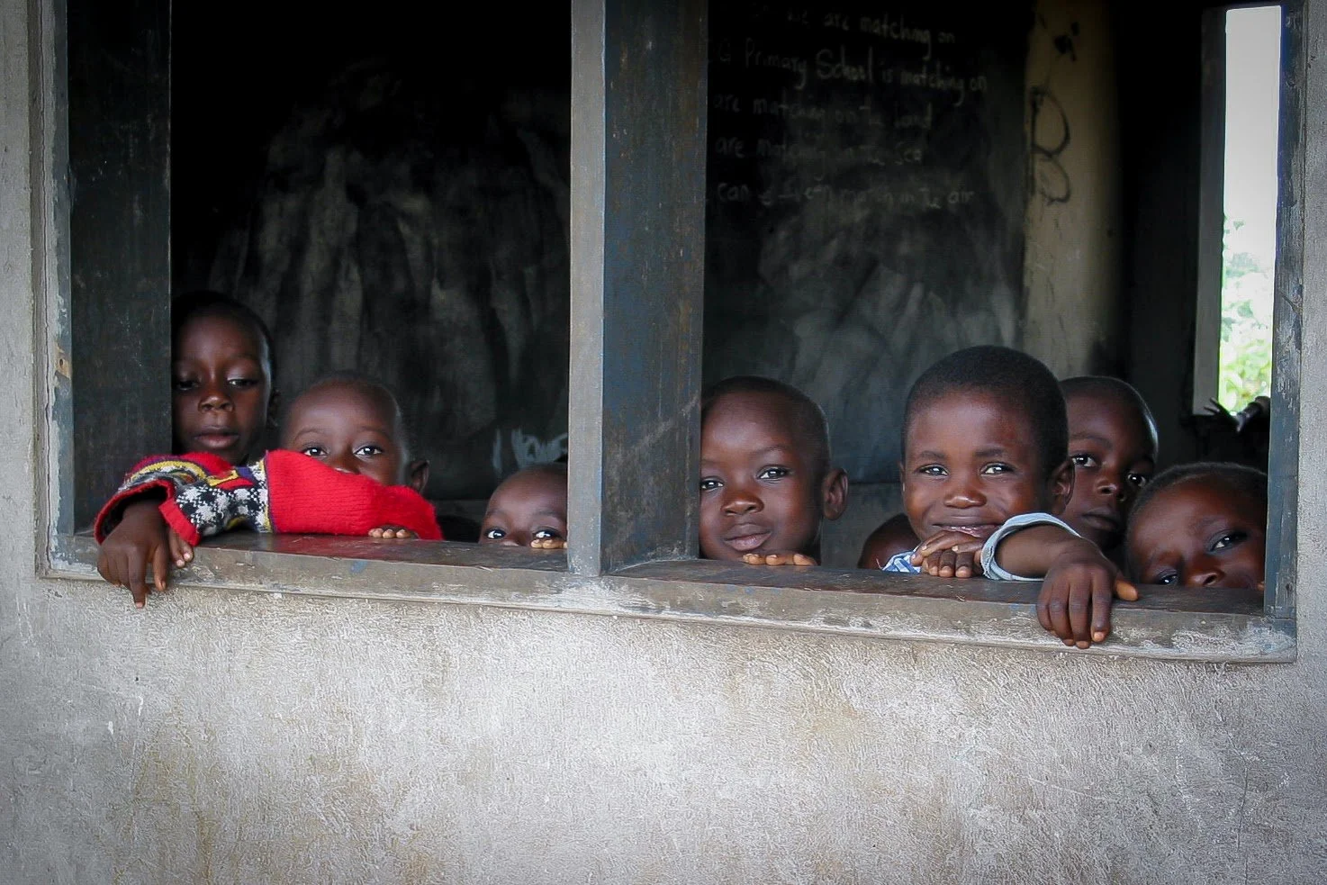 Children peering curiously out of a classroom window in a rural African school.