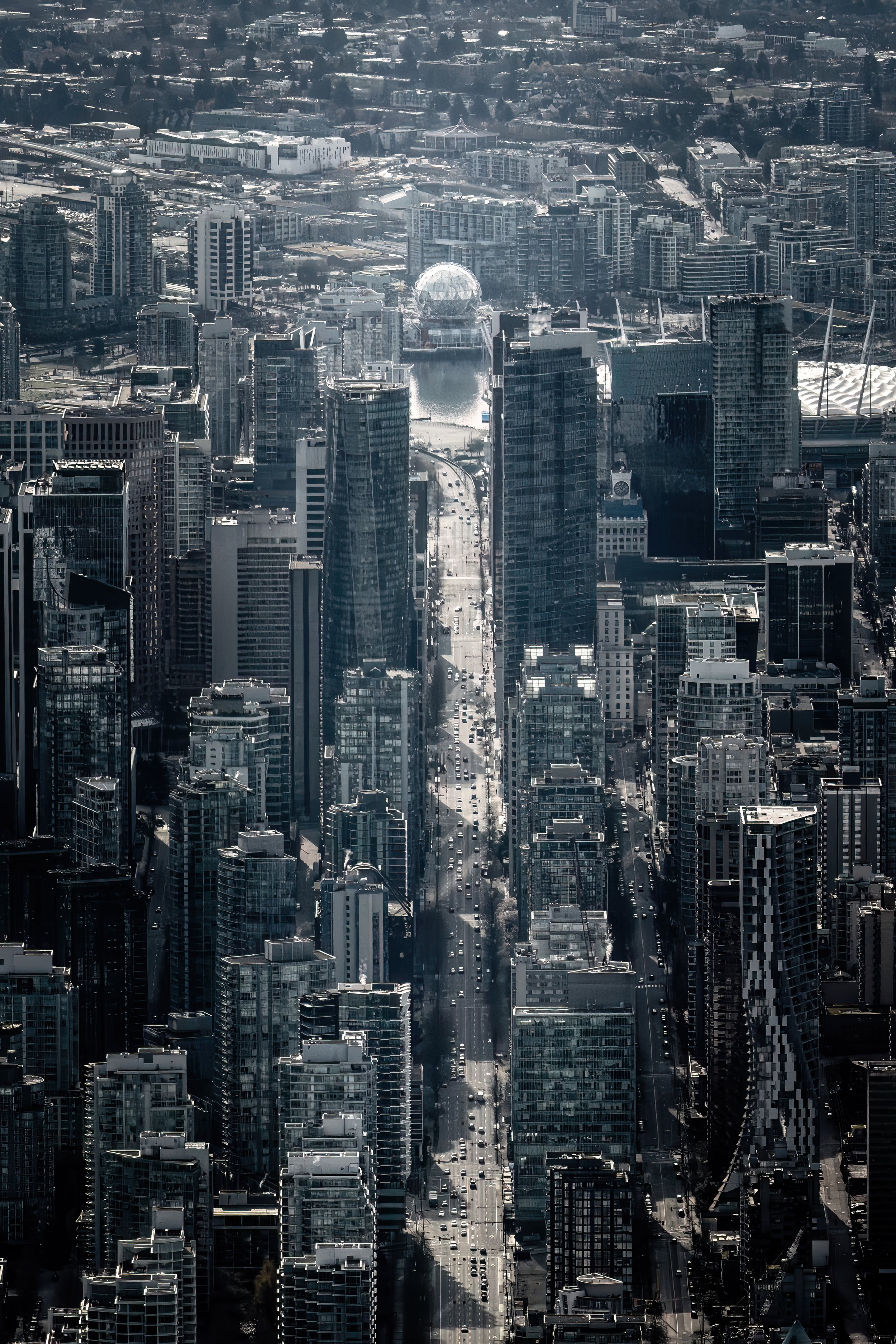A cityscape view of a densely packed urban area with numerous high-rise buildings, streets, and a body of water with a geodesic dome structure on the water's edge, under a clear sky. This image is copyrighted by Samuel Choy Photography.