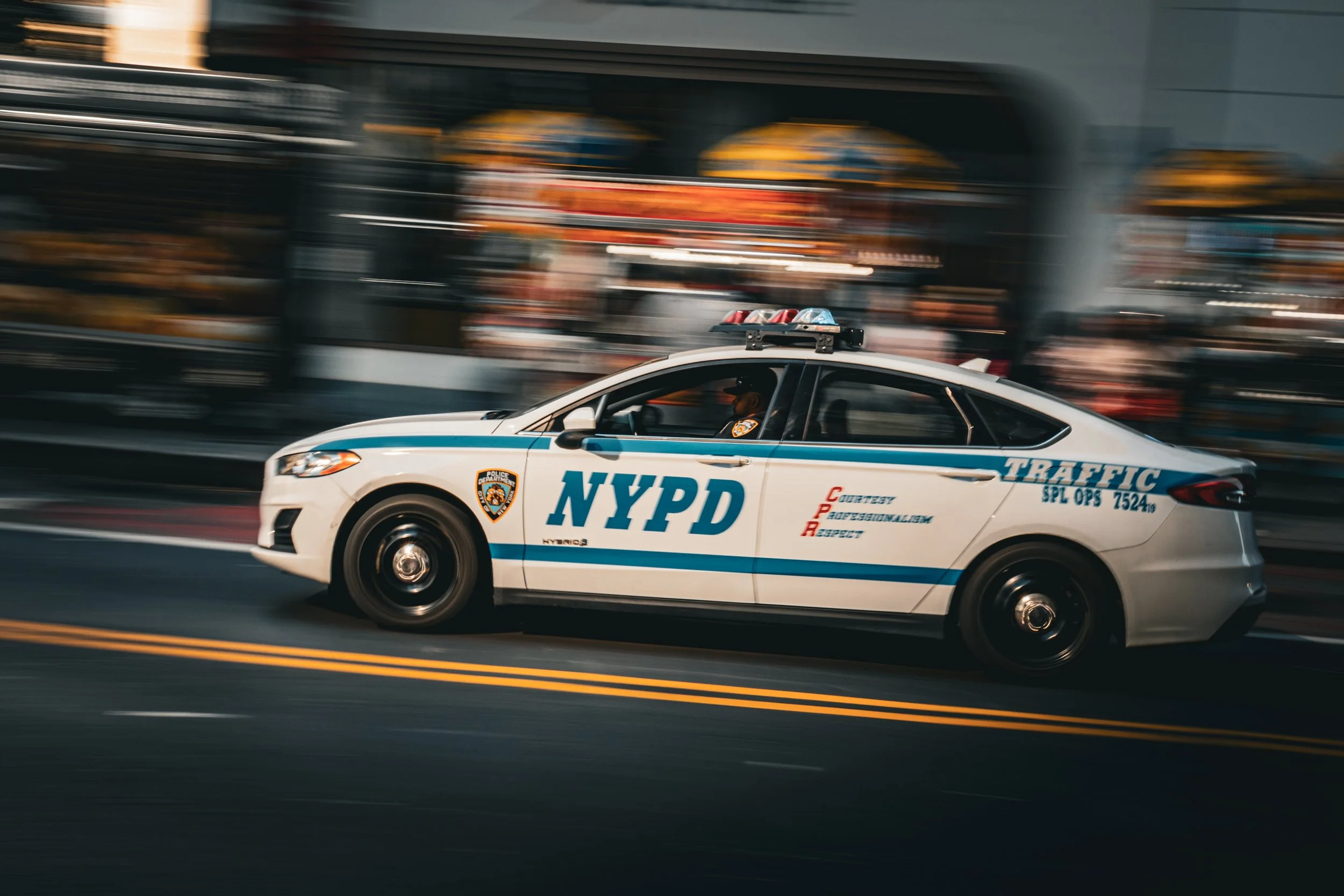 A police car from the New York Police Department (NYPD) speeding down a city street with blurred background.