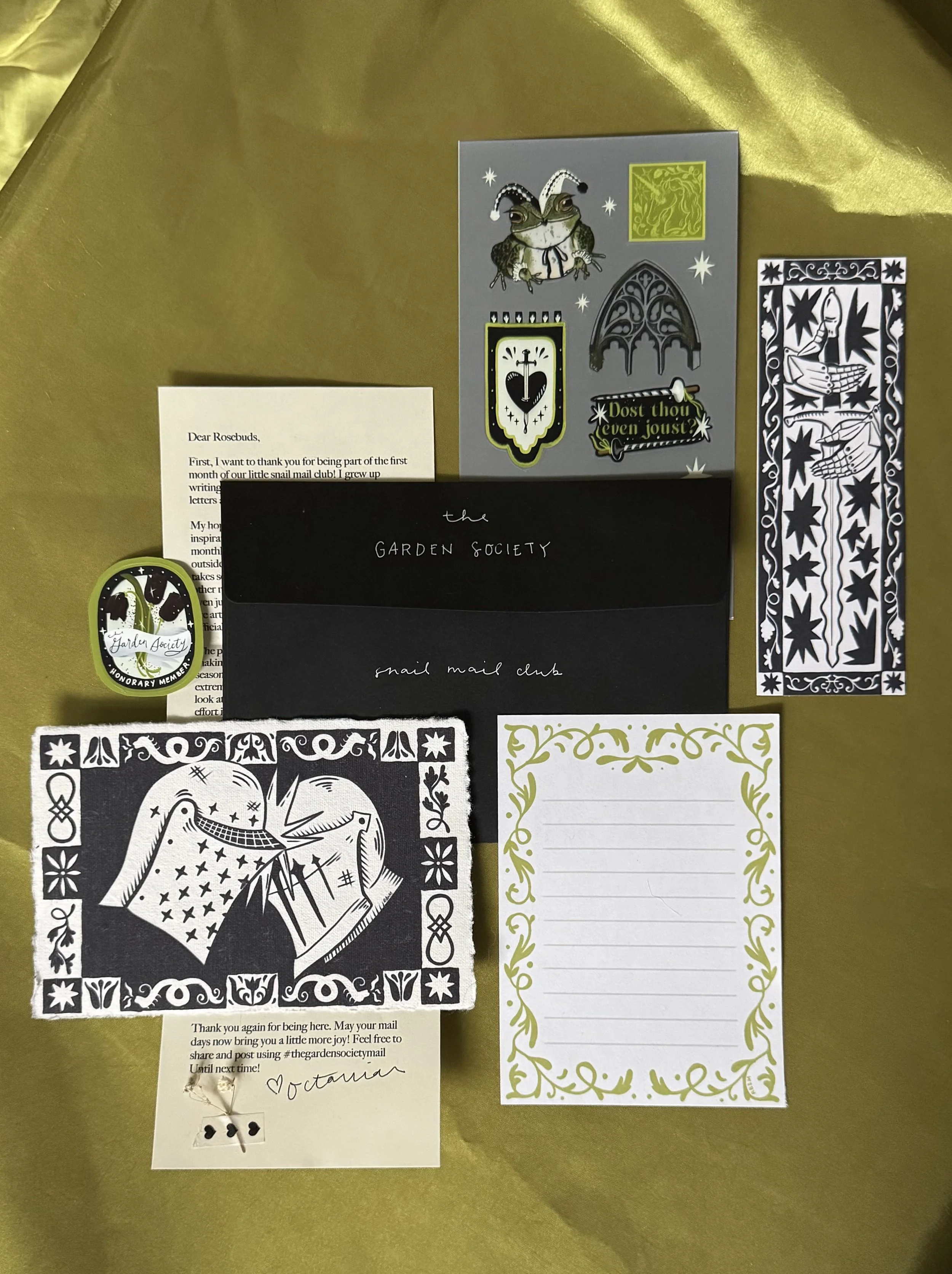 a flat lay photo of a medieval art print, sticker sheet, bookmark, and letter for the mail club theme of the month. 