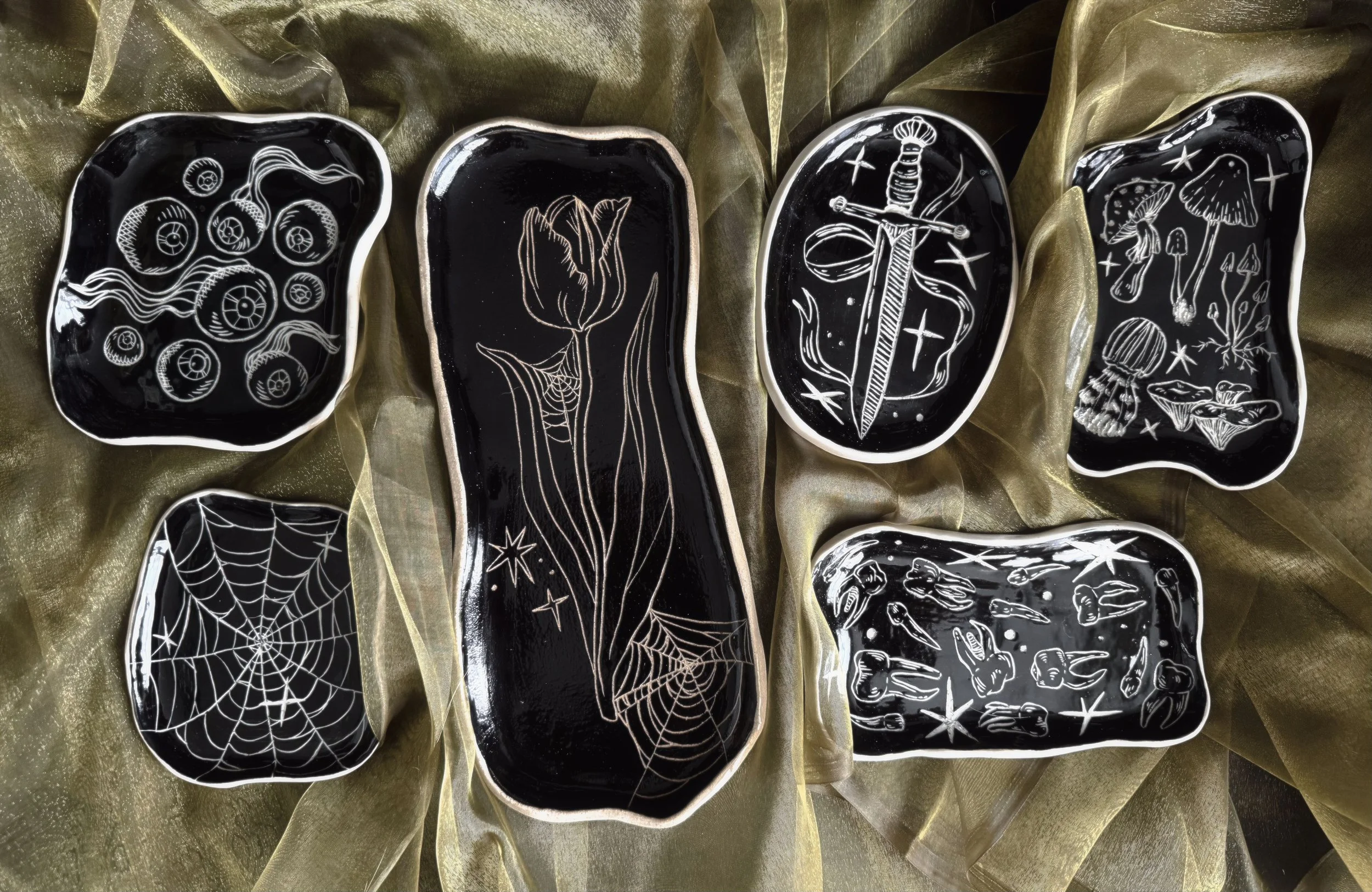 6 black ceramic plates with various spooky sgraffito style carvings.