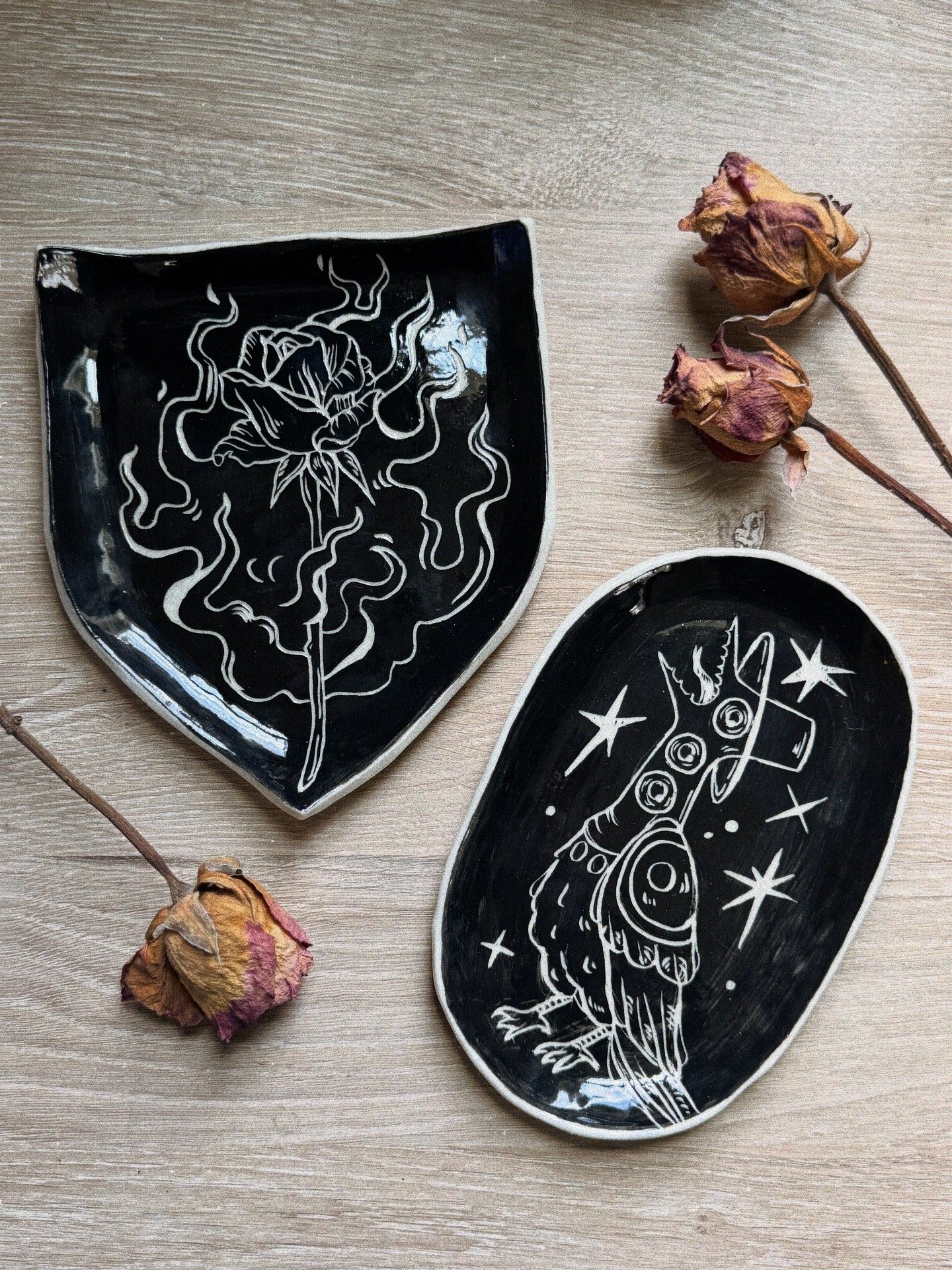 Two black ceramic plates with sgraffito carvings.