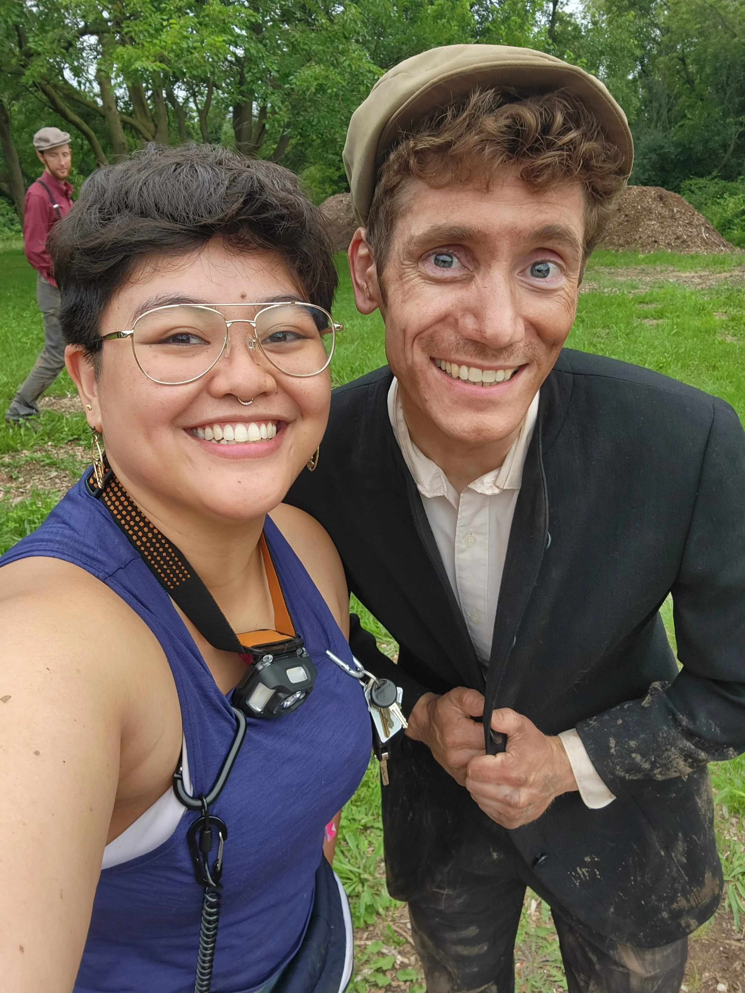 Regina, an Asian American woman smiles next to a white male actor covered in dirt.
