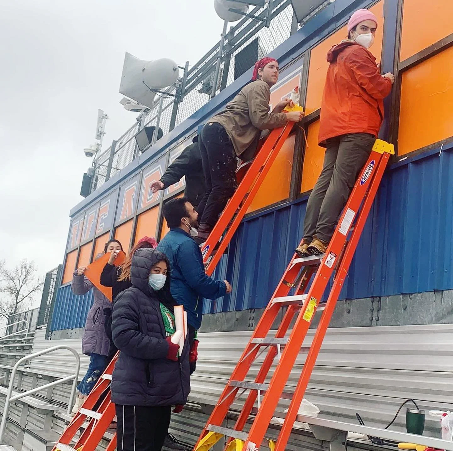 A group of people on ladders adding decorations to an outdoor set.