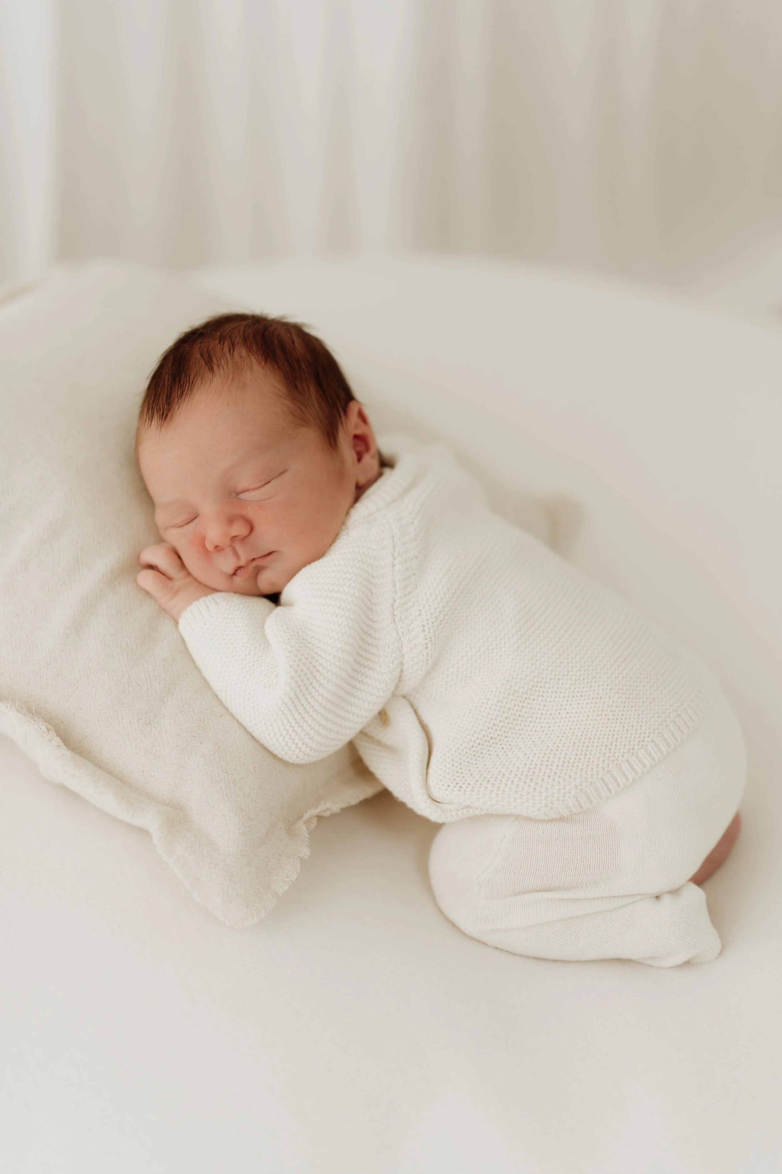 newborn baby curled up on tummy propped up by a pillow