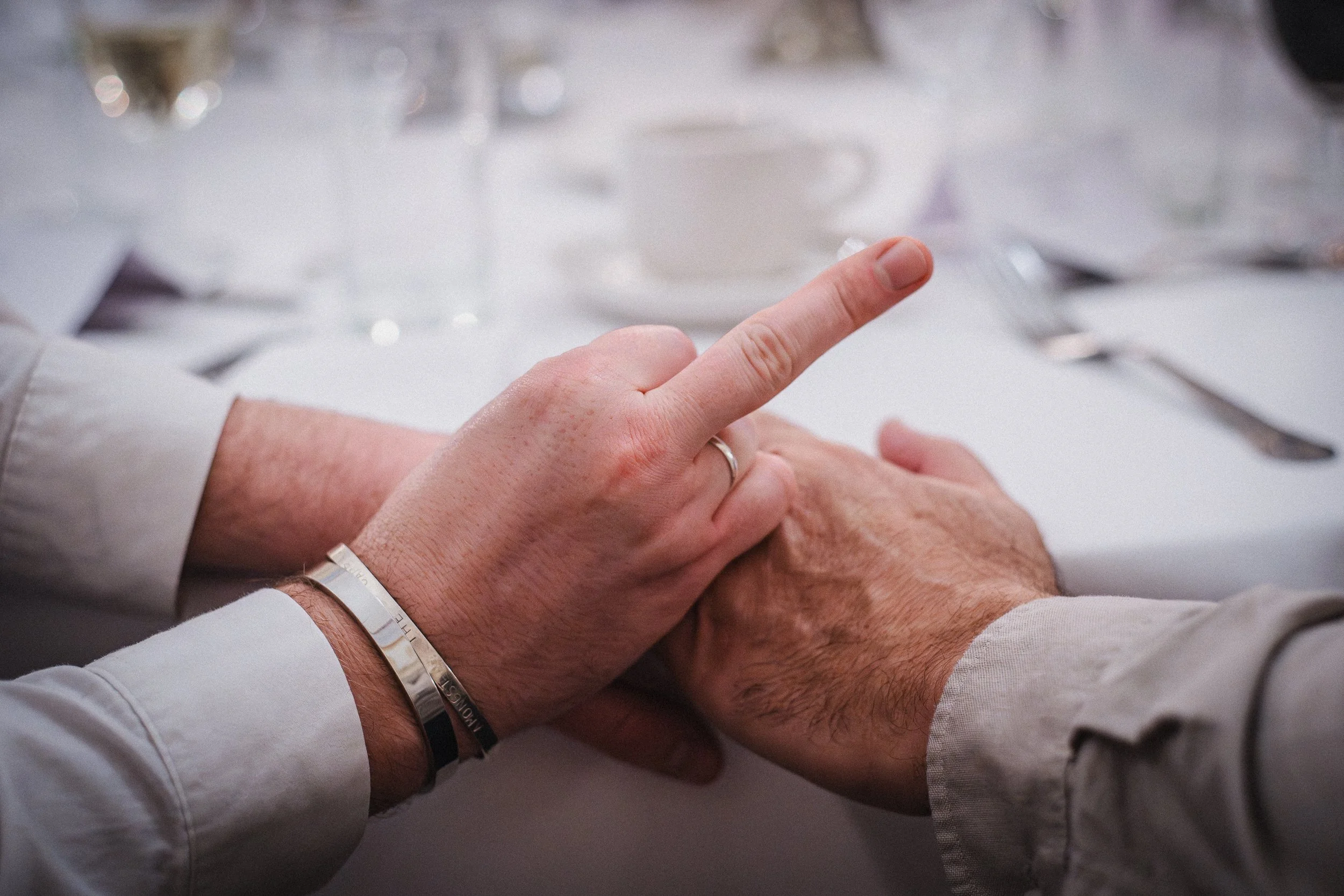 A person's hand touching another person's hand on a table, with a dining setting in the background.