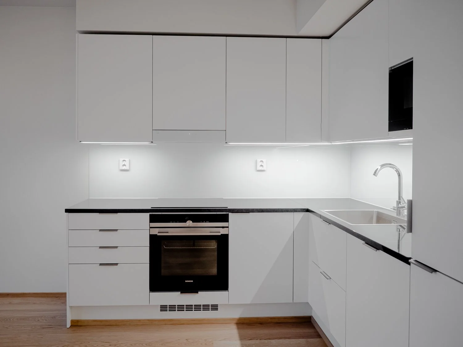 Modern kitchen with white cabinets, black countertop, built-in oven, and stainless steel sink.