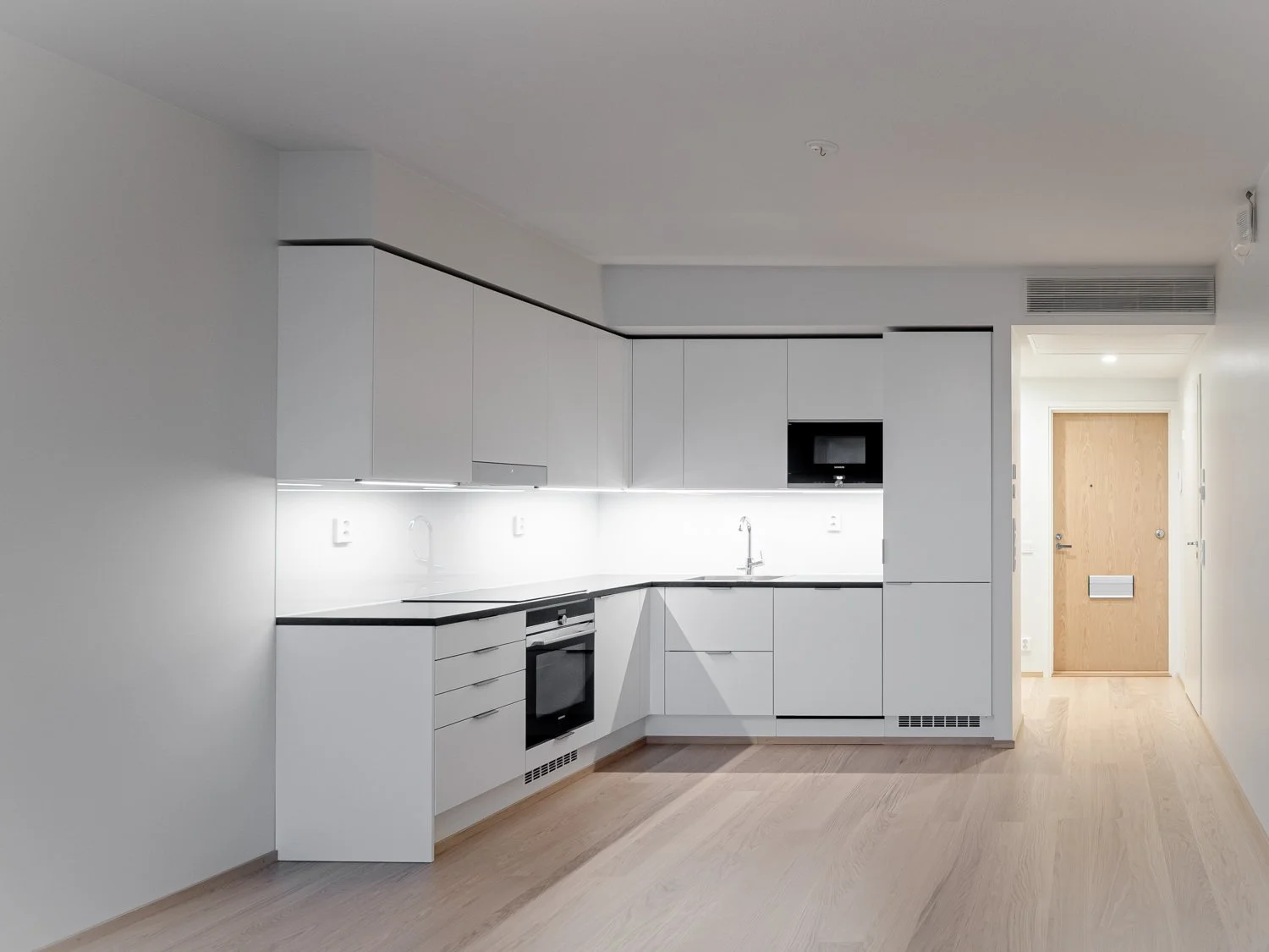 Minimalist modern kitchen with white cabinetry and wooden flooring.