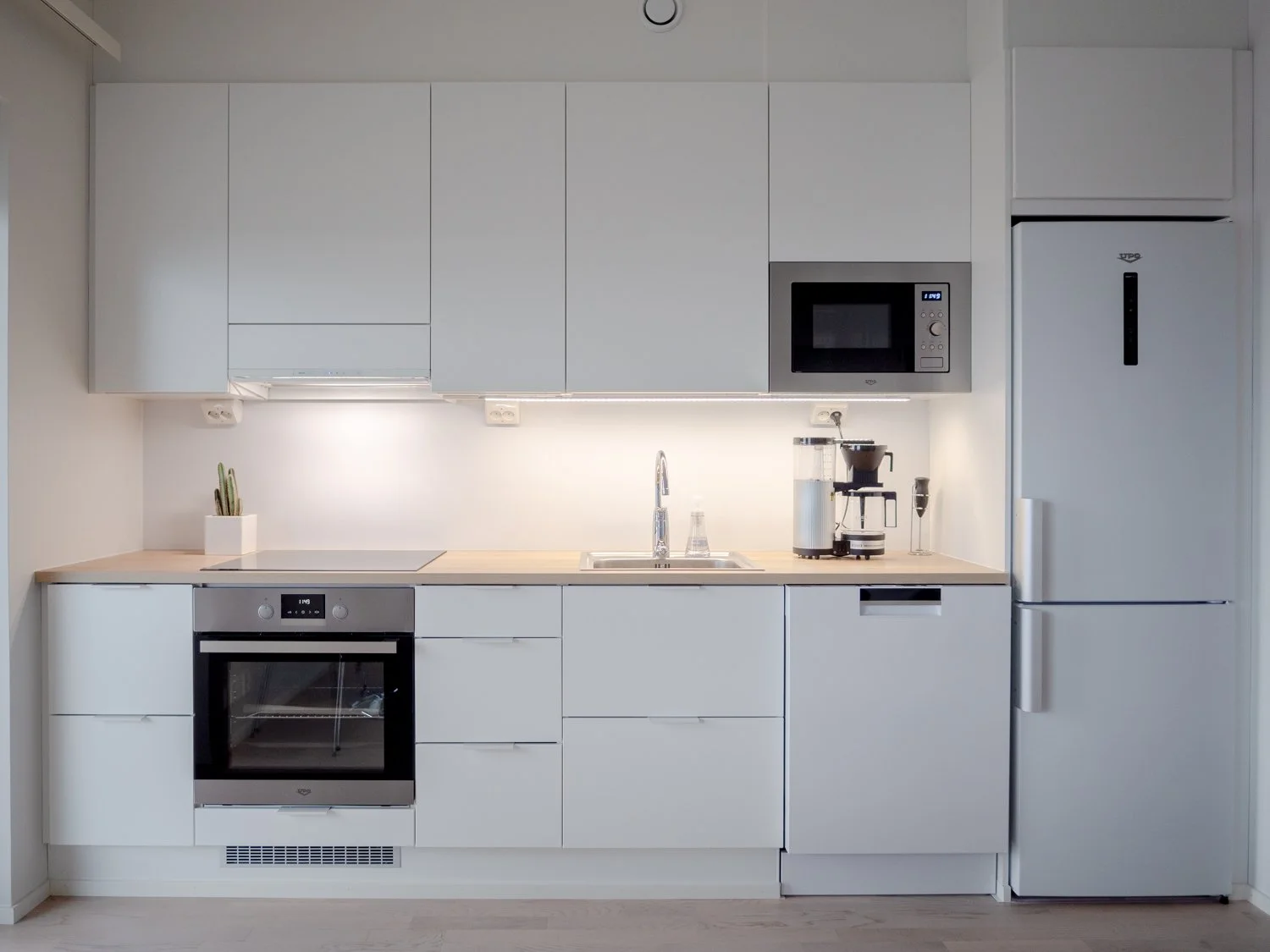 Modern kitchen with white cabinets, oven, microwave, fridge, and coffee maker