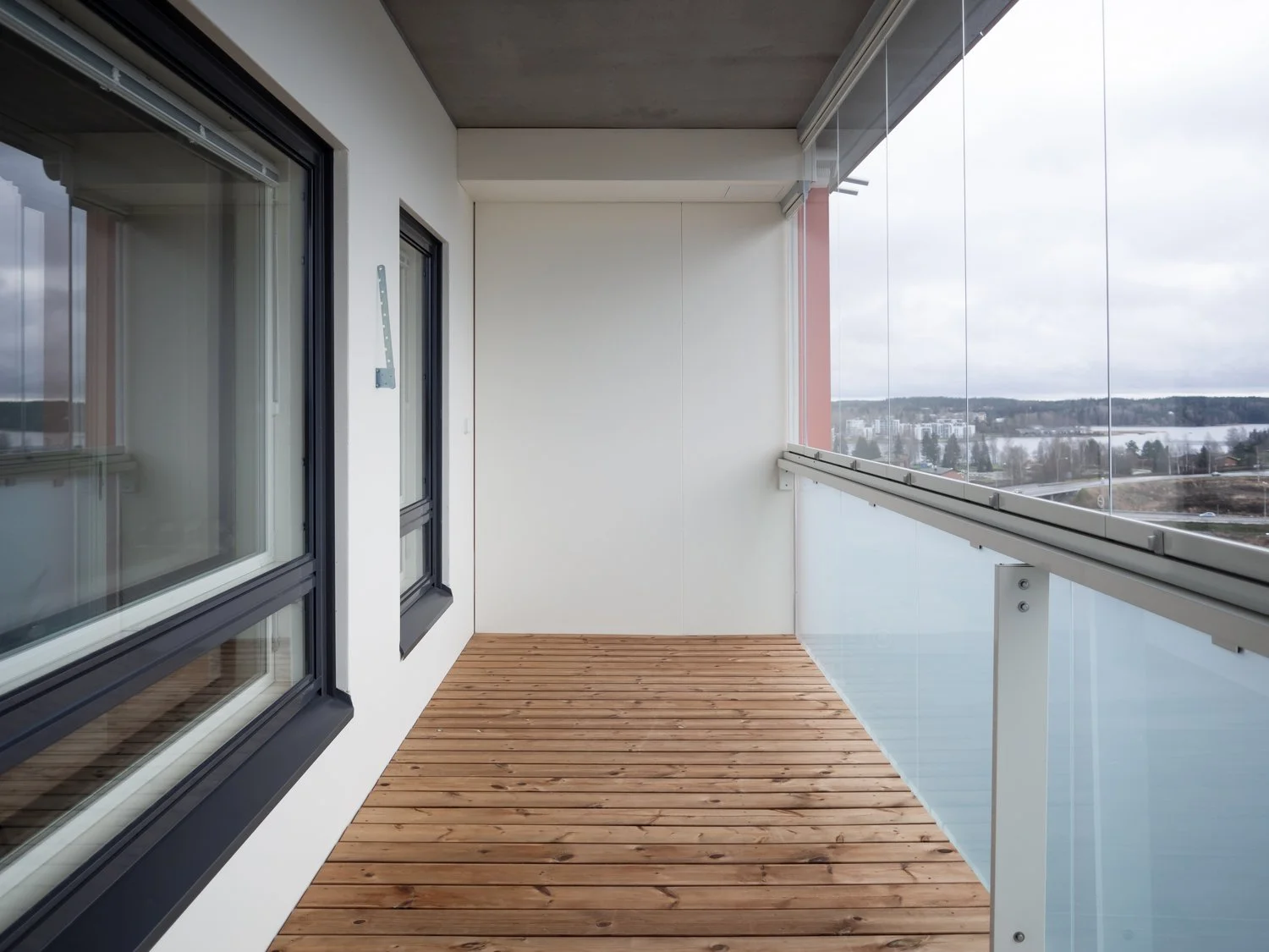 Modern glass-enclosed balcony with wooden flooring and scenic view.