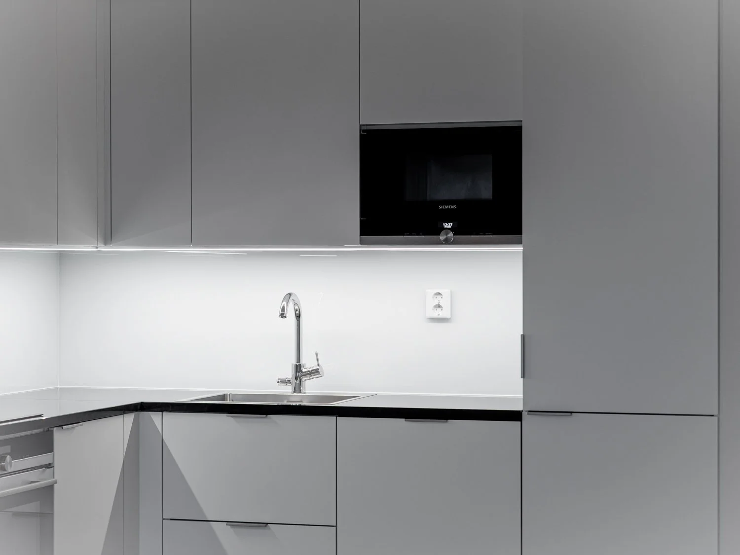 Modern kitchen with sleek grey cabinets, built-in Siemens microwave, stainless steel faucet, and minimalistic design.