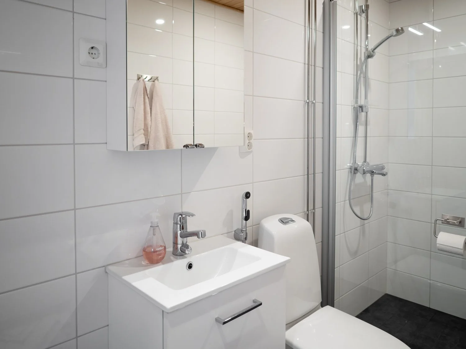 Modern white bathroom interior with sink, mirror cabinet, toilet, towel, and glass shower enclosure.