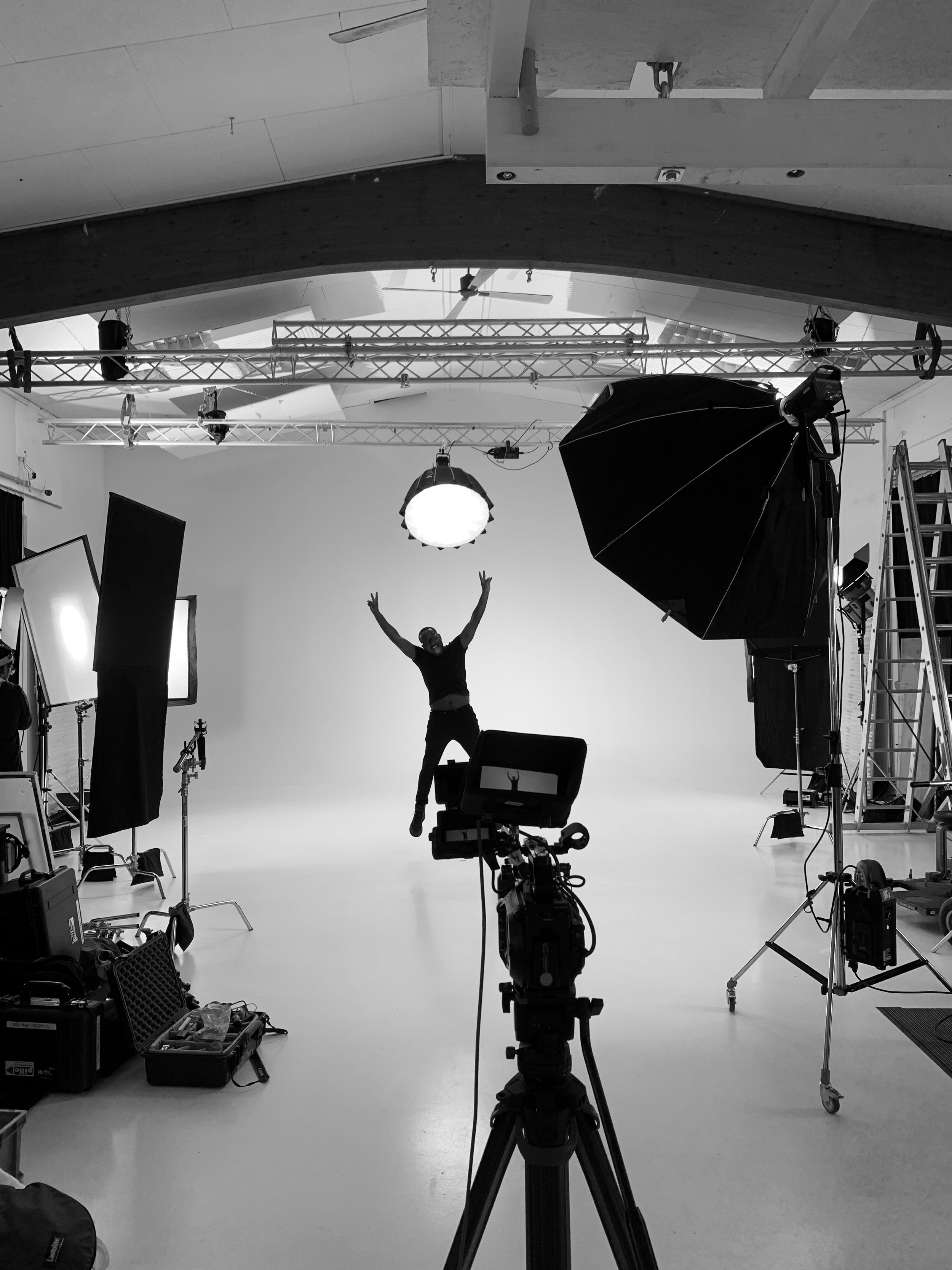 Black and white photo studio with camera equipment, lights, and a person jumping in the center.