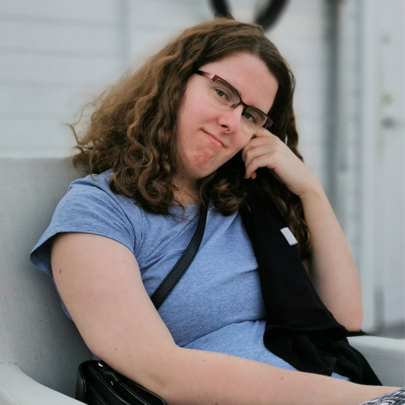 Marina Andersson med långt, lockigt hår och glasögon, bär en blå T-shirt och ser nyfiken ut.