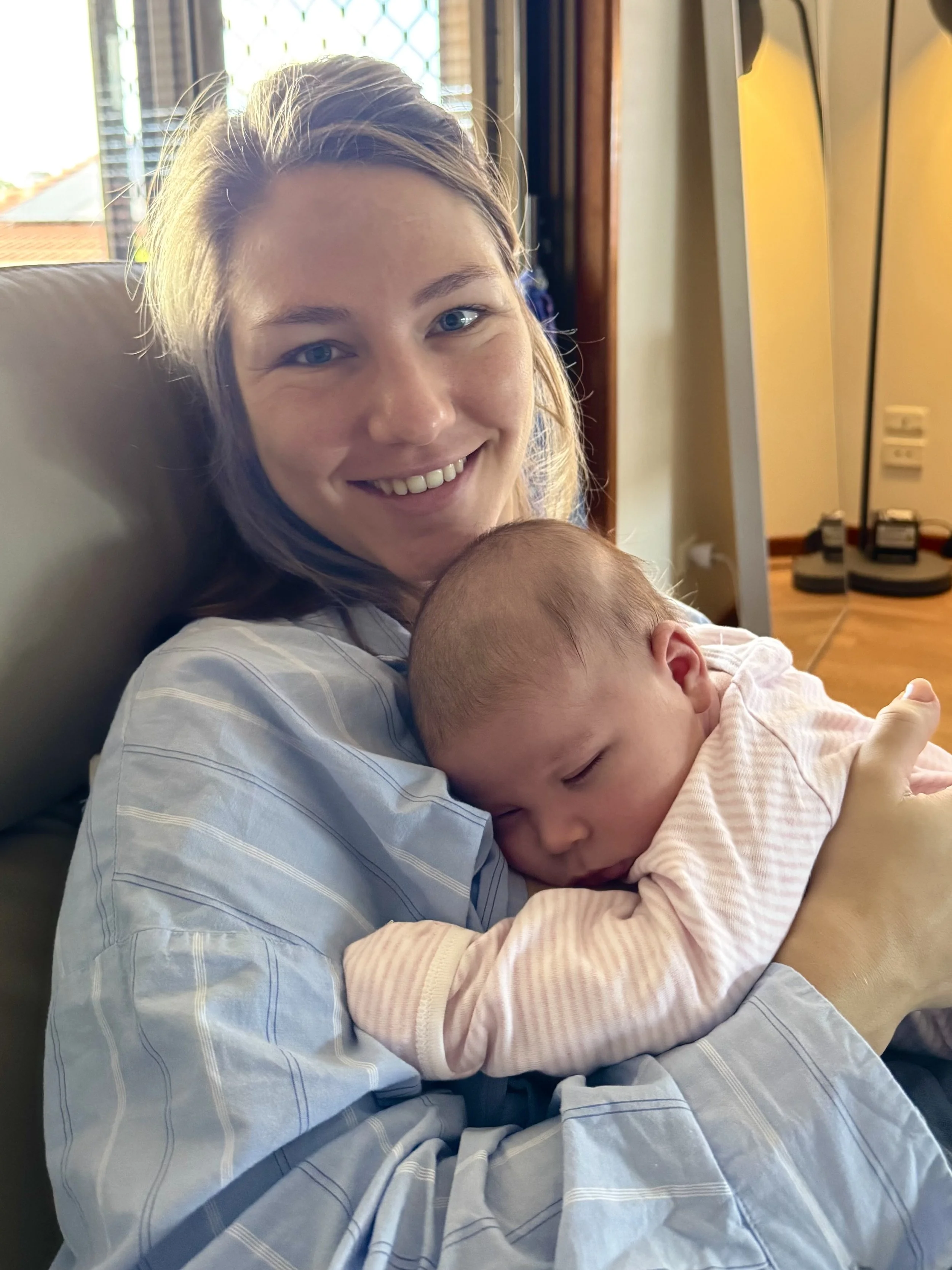 A new mother smiling while holding a sleeping baby.
