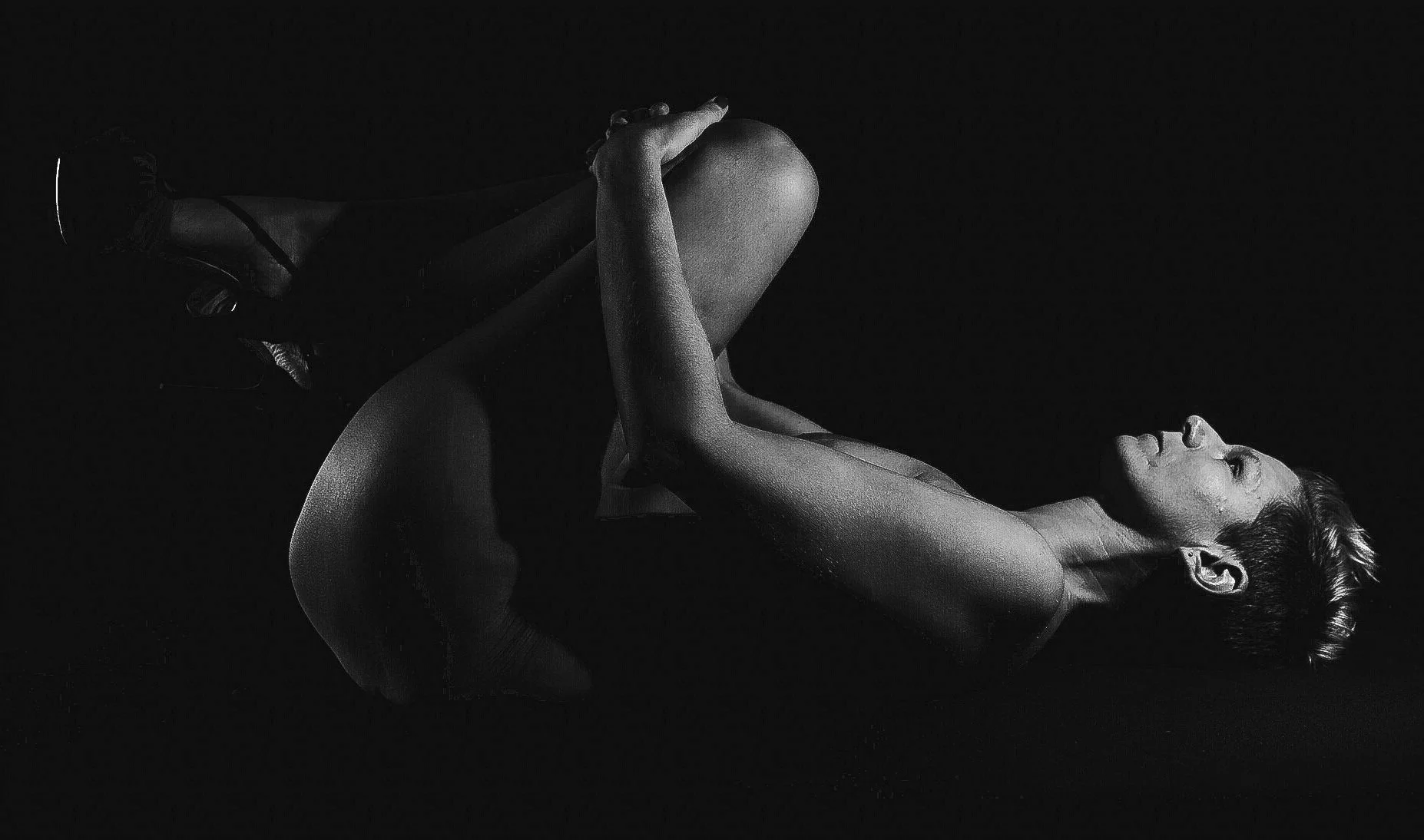 Femme en position de yoga ou méditation en noir et blanc, avec lumière contrastée mettant en valeur sa silhouette.