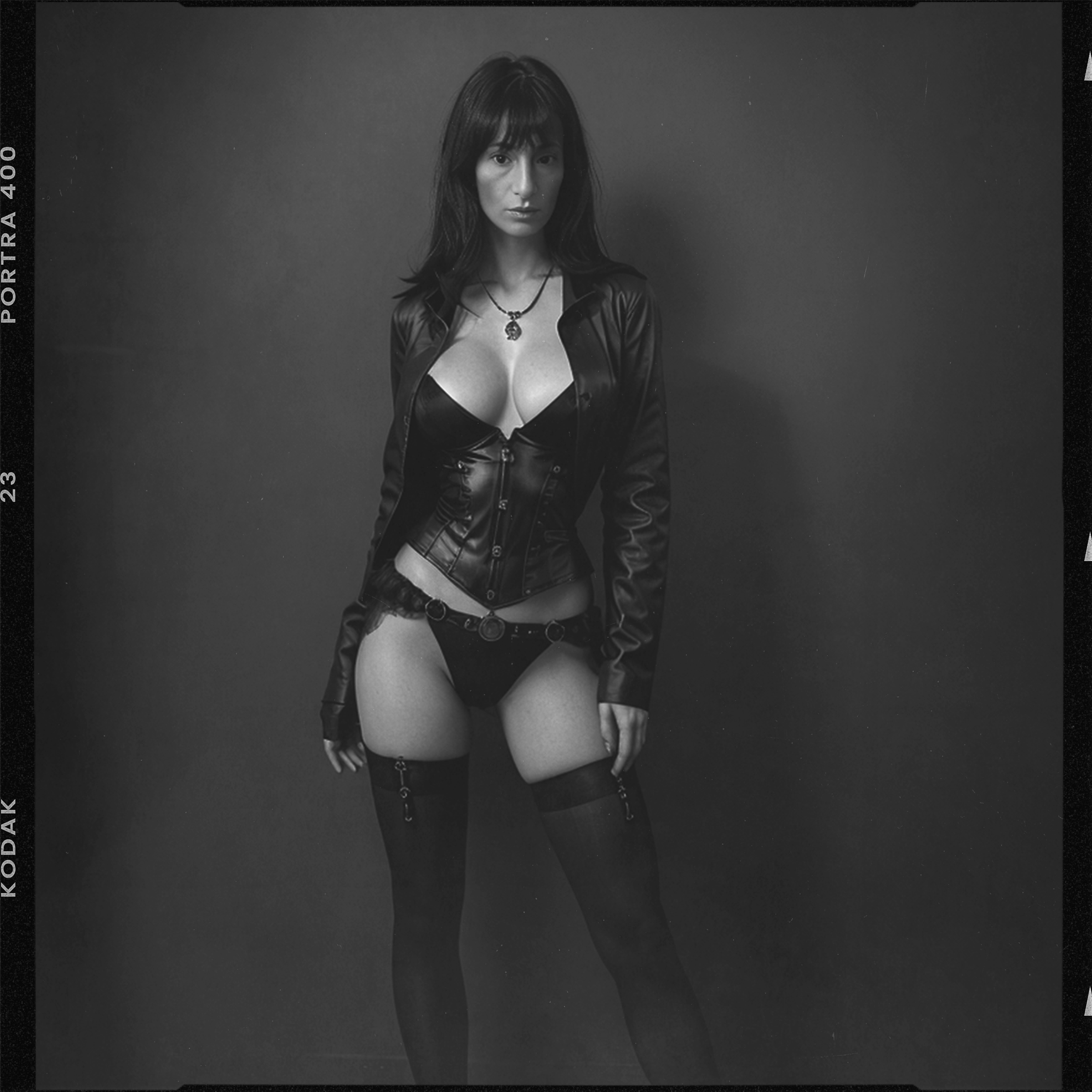 Une femme posant en lingerie et veste en cuir noir, portant des collants noirs et une chaîne à la taille, dans une photo en noir et blanc.