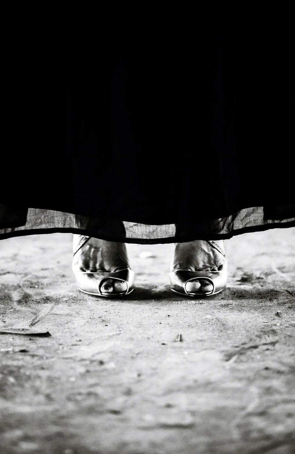 Semelles de chaussures visibles sous une longue robe ou jupe, vue de dessous en noir et blanc.