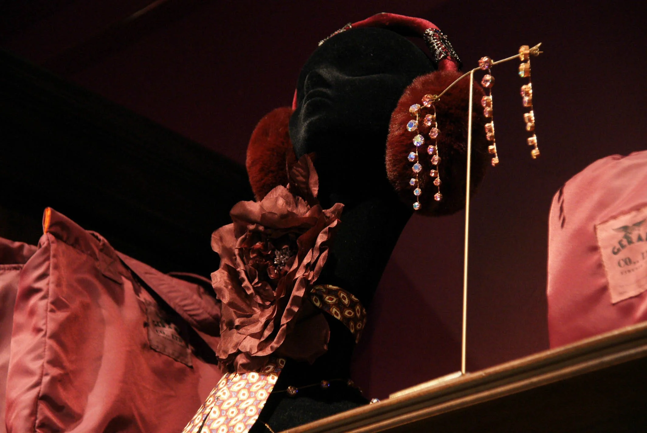 A Gerard Antwerp mannequin head wearing a black velvet hat decorated with beads, feathers, and brooches, displayed on a shelf with pink packaging.