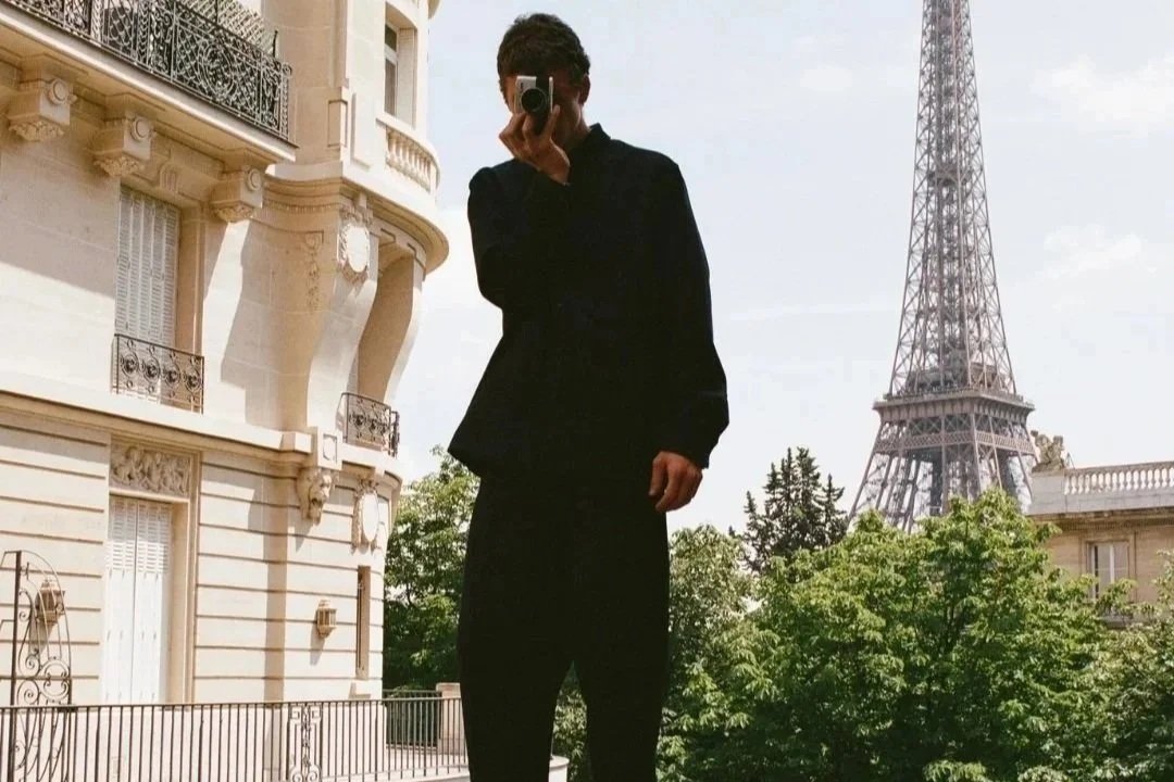 Person taking a photo in front of a building with the Eiffel Tower in the background.