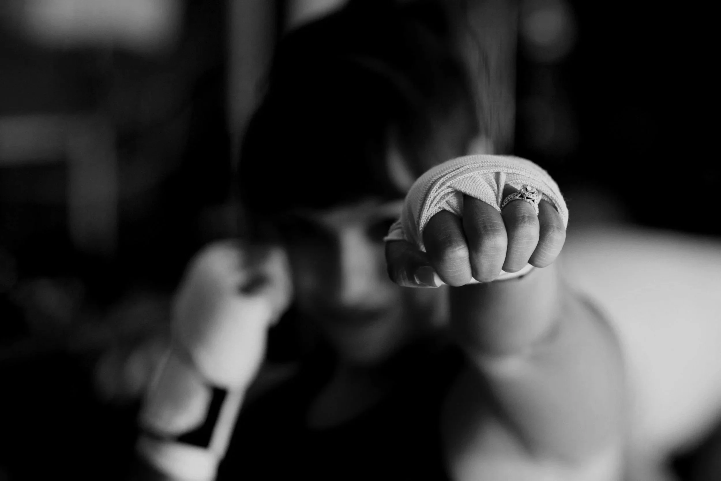 Eine Frau macht einen Boxer-Schlag in ein schwarzes und weißes Foto, trägt eine Bandage am Handgelenk.