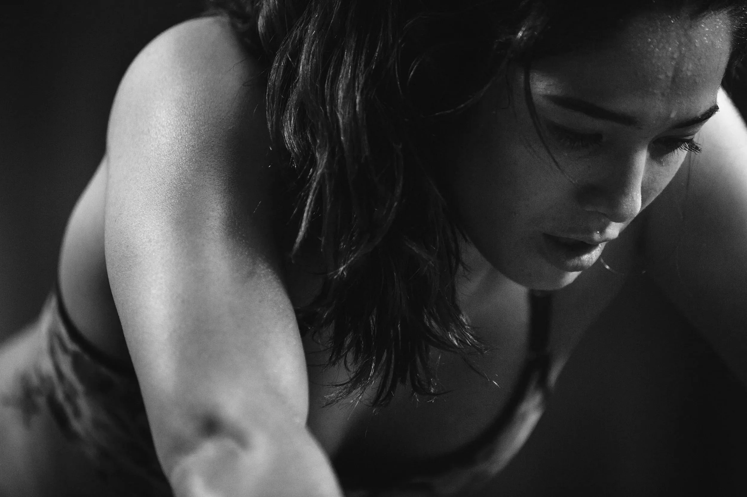 Schwarz-weiß-Foto einer sportlich aussehenden Frau, die sich beim Training anstrengt, mit nassen Haaren und Schweiß im Gesicht.