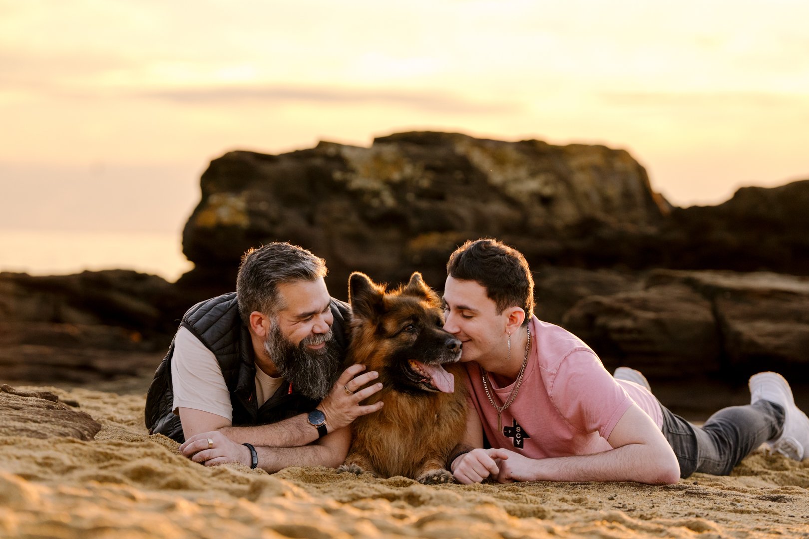 Dan and Josh lying on the sand either side of Dexter at Royal Beach, Mornington