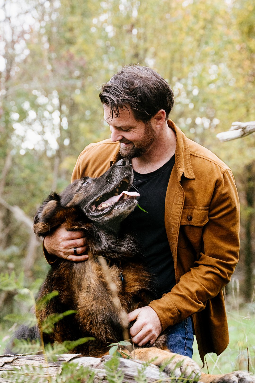 Joel cuddling Archie on a fallen log while the ten year old German Shepherd grins up at him