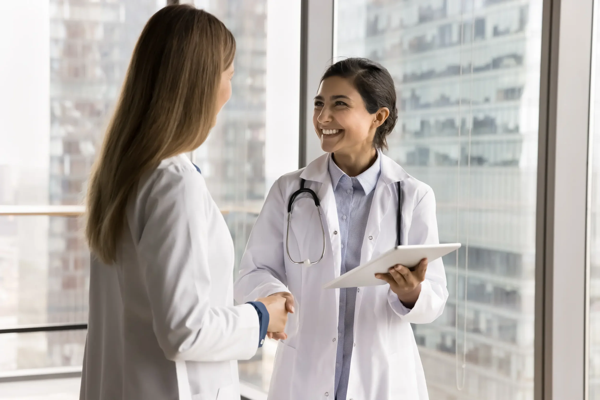 Zwei lächelnde Ärztinnen schütteln sich die Hände