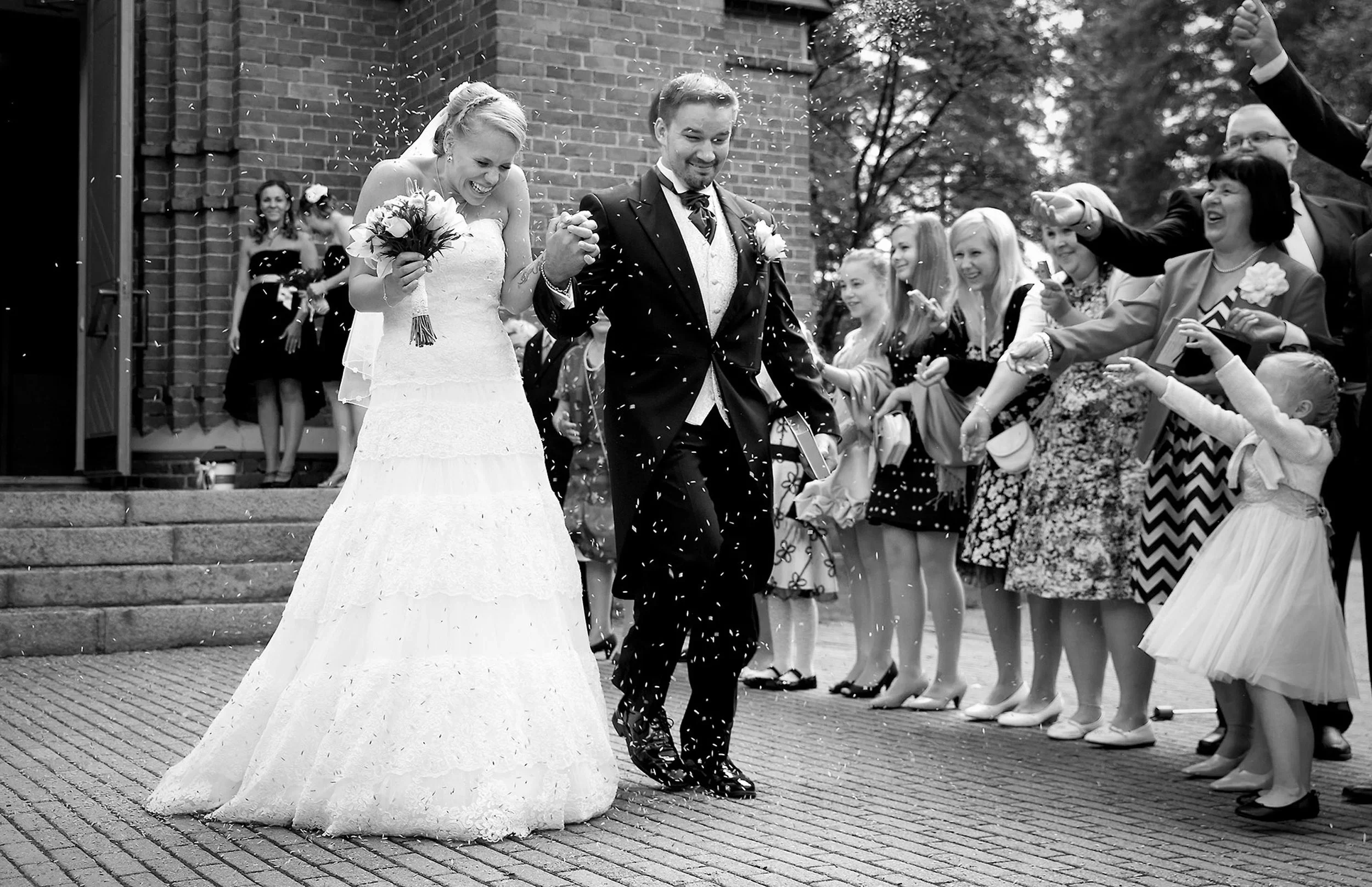 Hääpari kävelee ulos kirkosta, ihmiset heittävät riisiä, naurua ja iloa, taustalla kirkko.