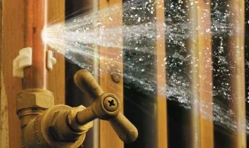 A broken pipe spraying water through wooden slats.