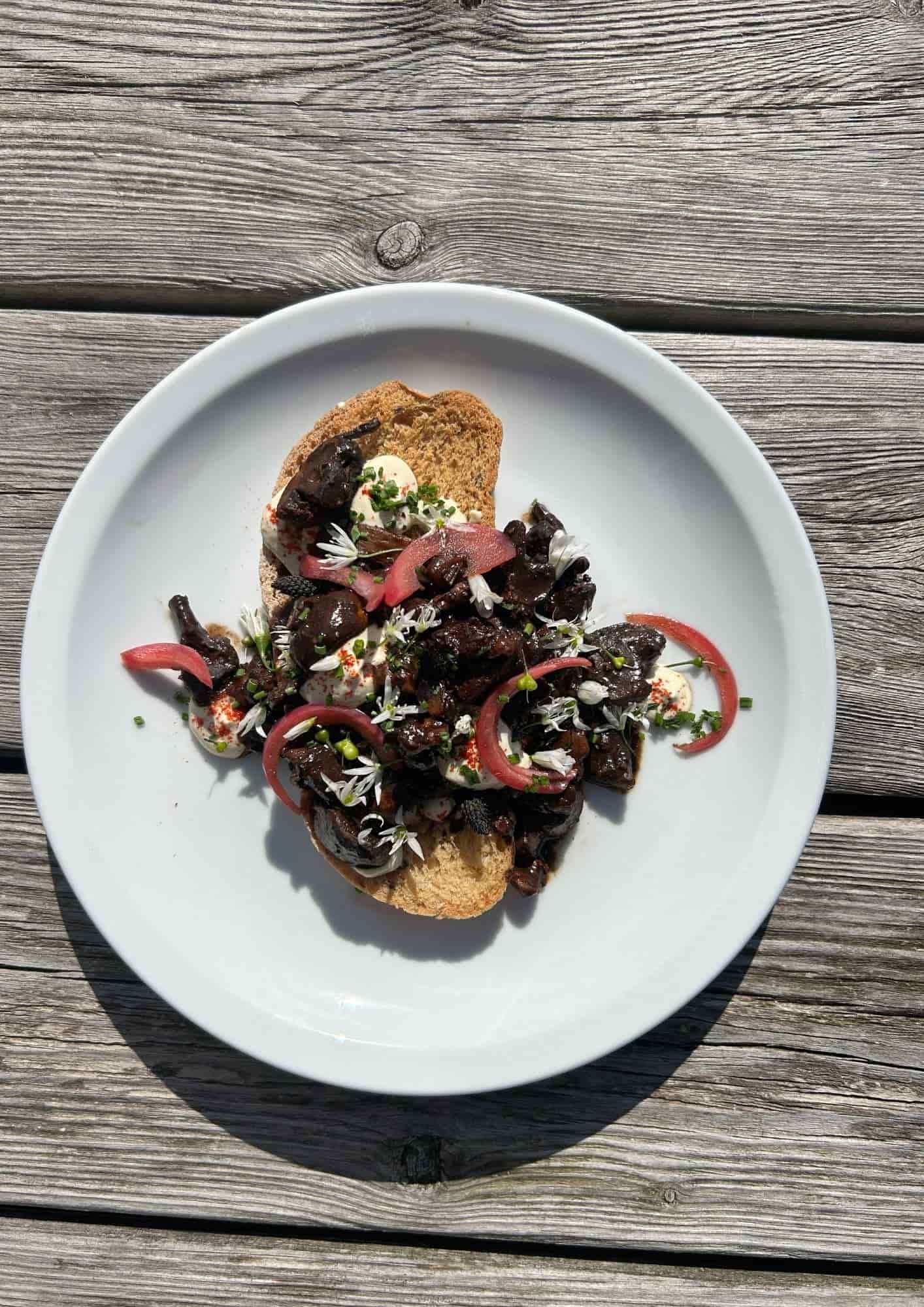 Earthly Feasts retreat catering. Open-faced sandwich with dark sautéed mushrooms, pickled onions, fresh herbs, and edible flowers on whole grain bread.