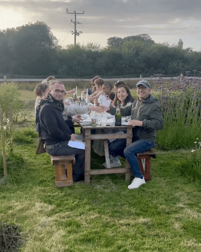 people smiling around a long bench table in a flower field