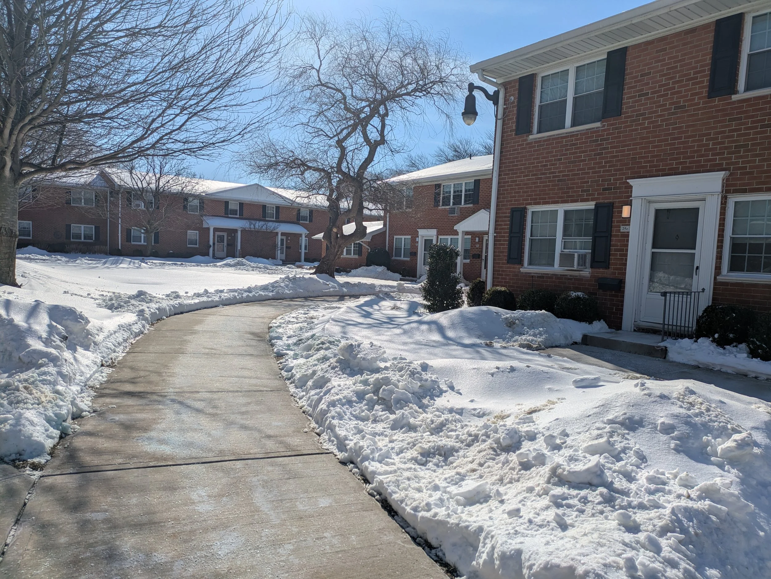 Courtyard of a red brick apartment complex with a clear sidewalk path through the snow.