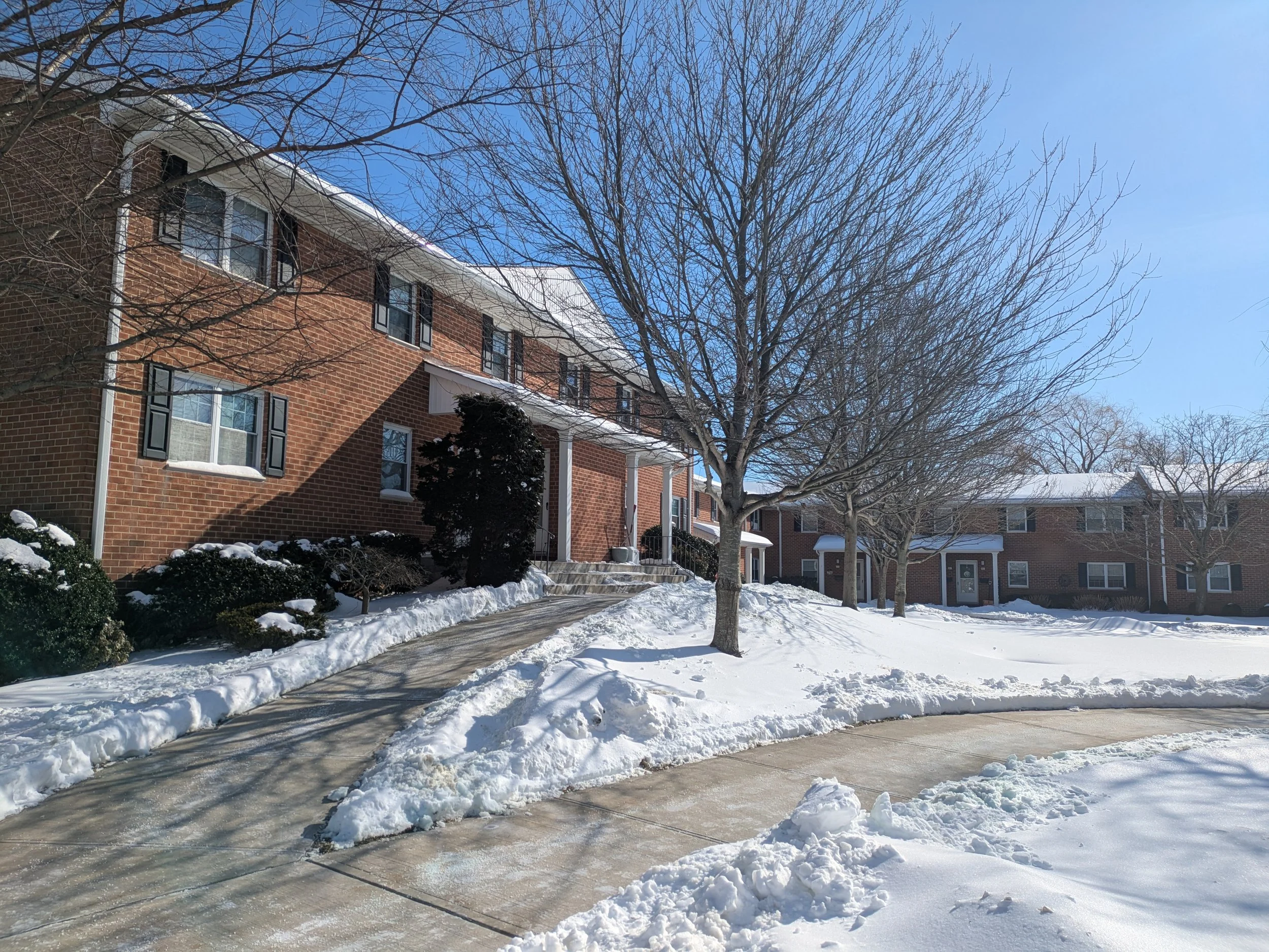 Red brick apartment building with a sidewalk path dug out between drifts of snow.