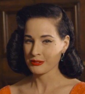 A woman with dark wavy hair styled in a vintage 1940s look, wearing red lipstick and a red outfit, with a confident expression.