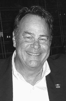 A smiling man with dark hair, wearing a white shirt and blazer, in an indoor setting.