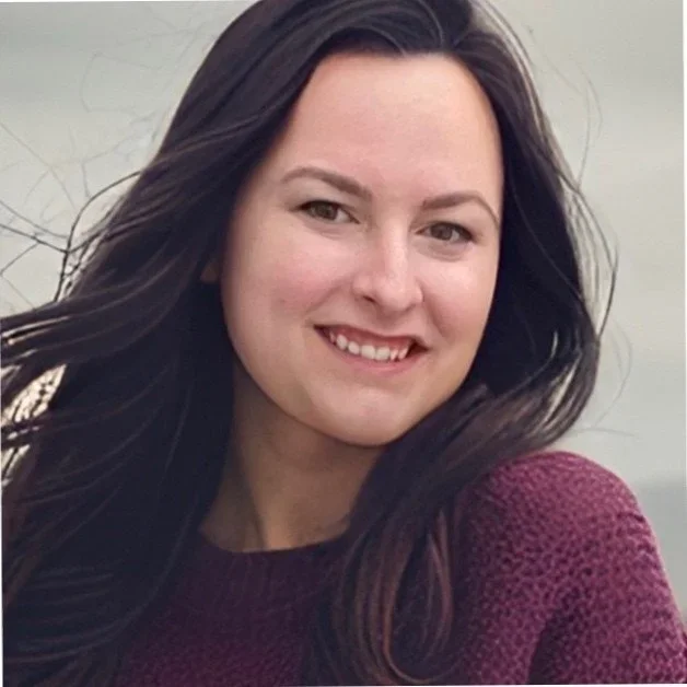 A woman with long dark hair smiling at the camera, wearing a maroon sweater.