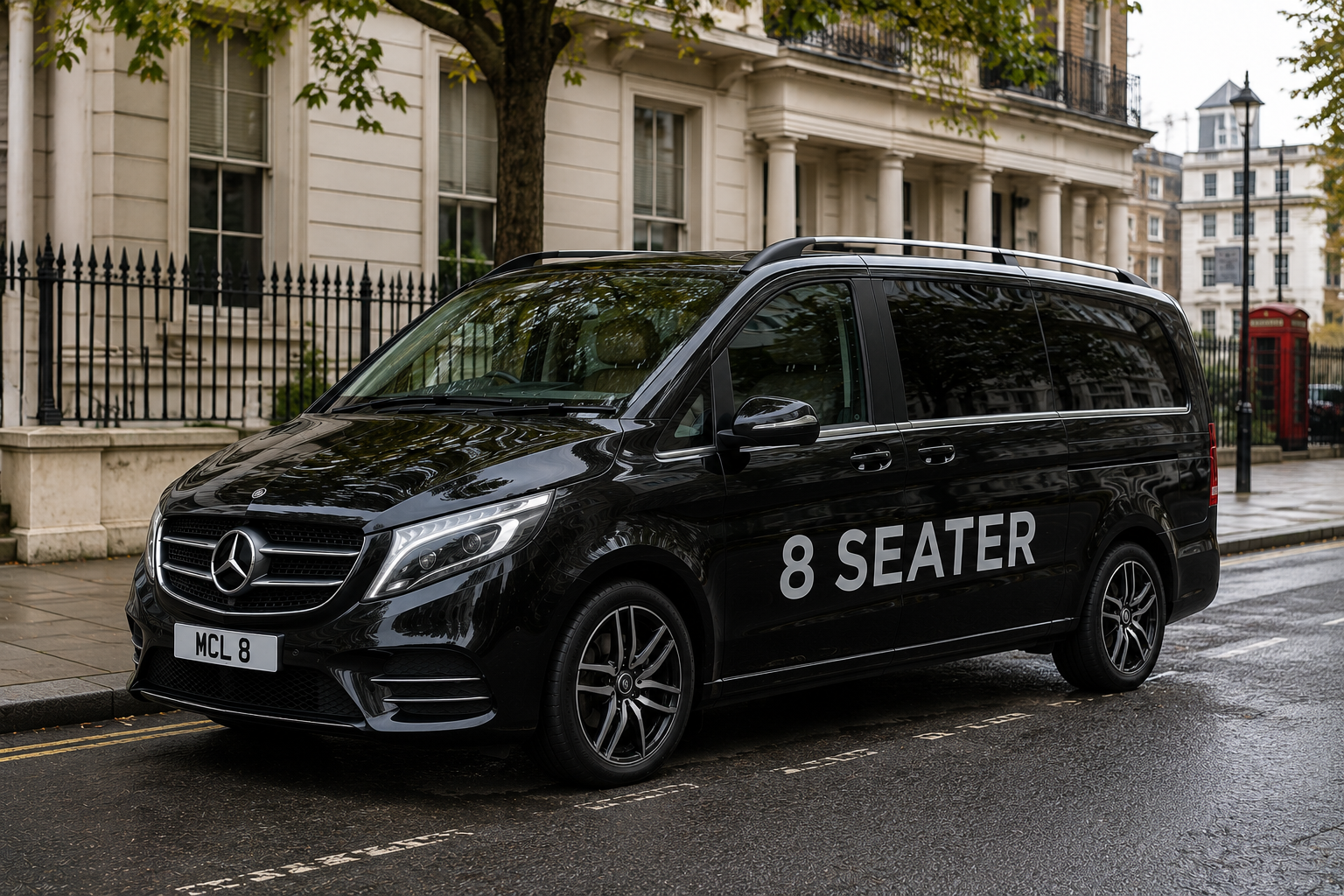 Black Mercedes-Benz van with '8 SEATER' lettering parked on wet city street in front of a residential building with white facade and black iron fence.