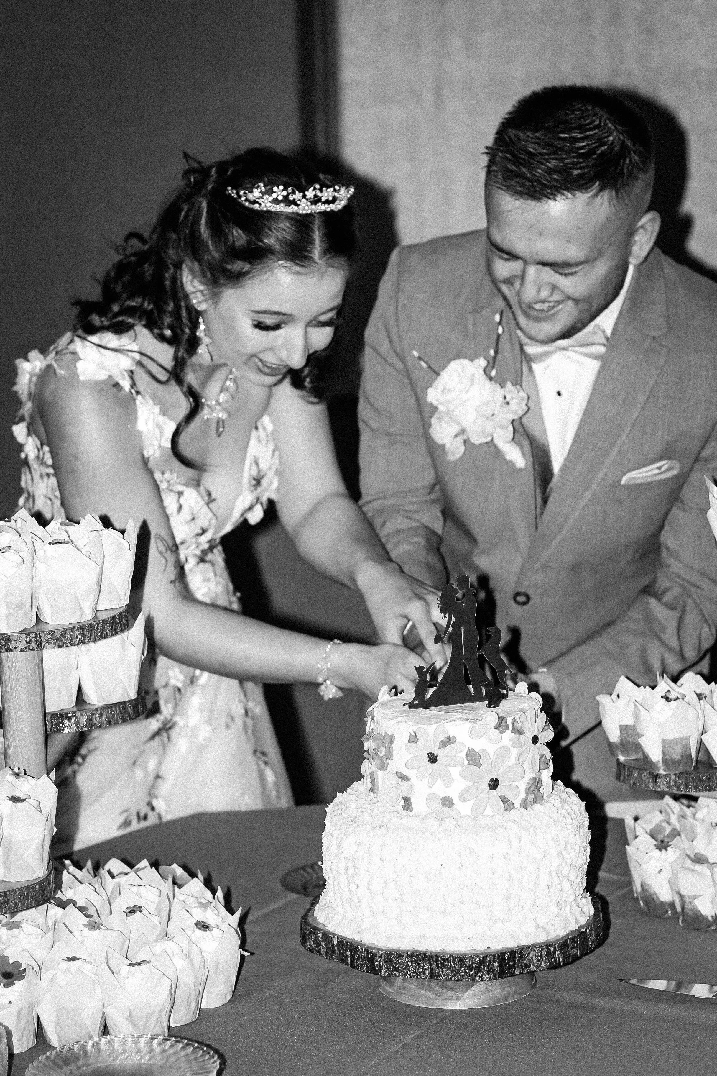 A bride and groom cut a wedding cake together at their wedding reception.